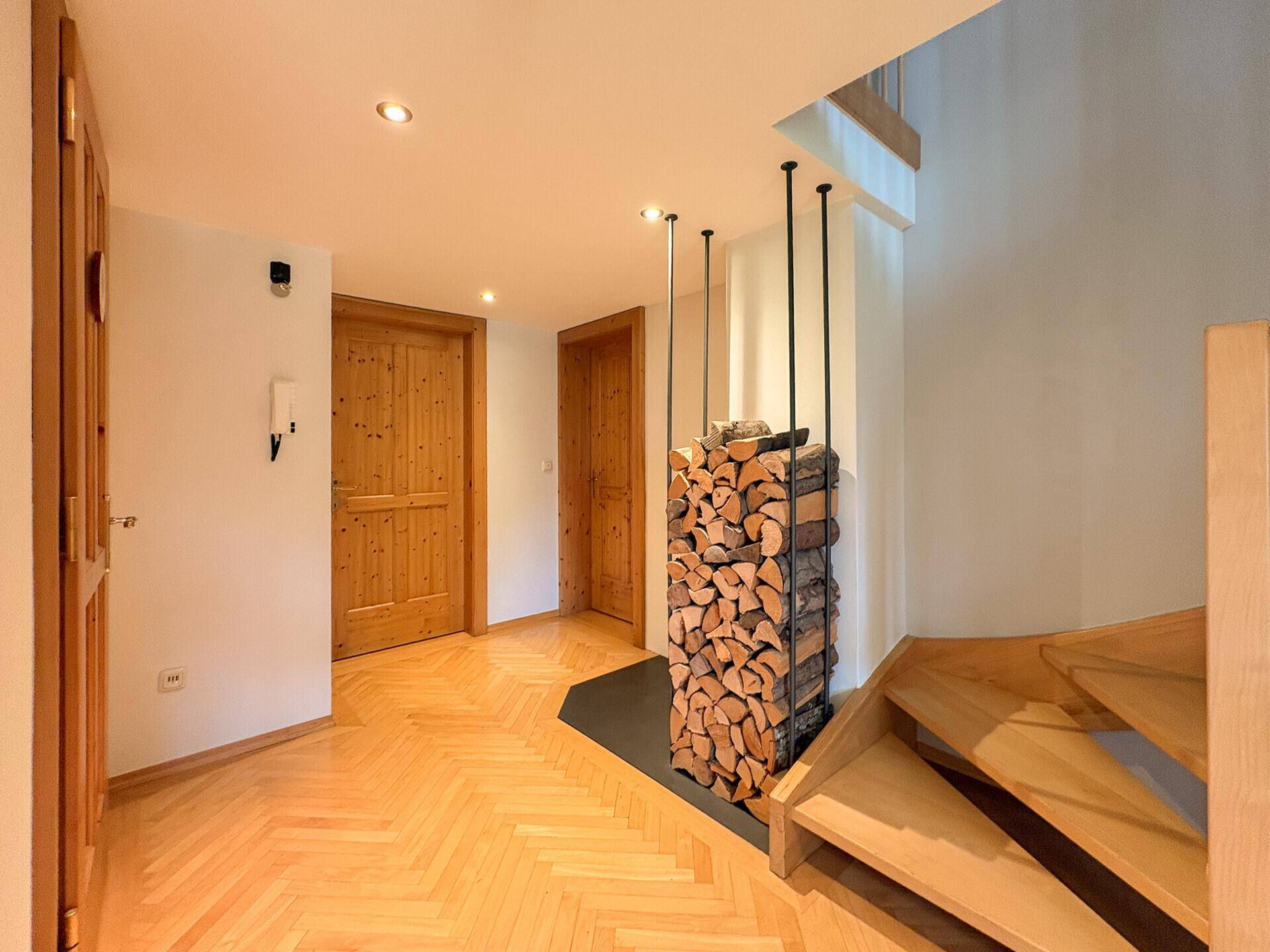 Eingangsbereich mit Holzparkett, offener Holzstapelung und Holztreppe.