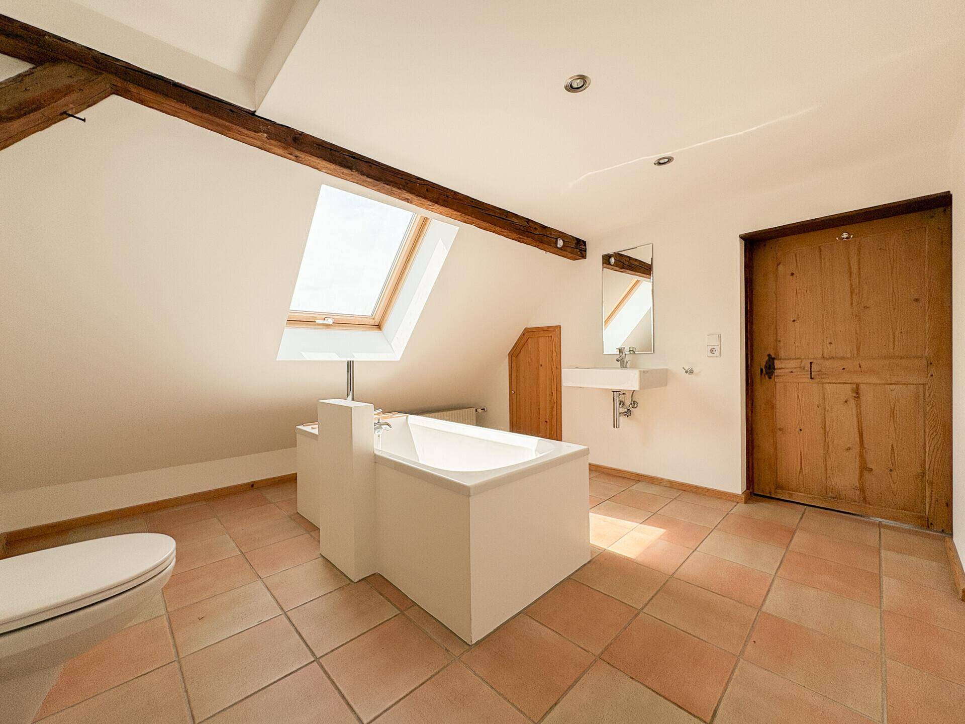 Modernes Badezimmer im Dachgeschoss mit Badewanne, Dachfenster und Holzbalken.