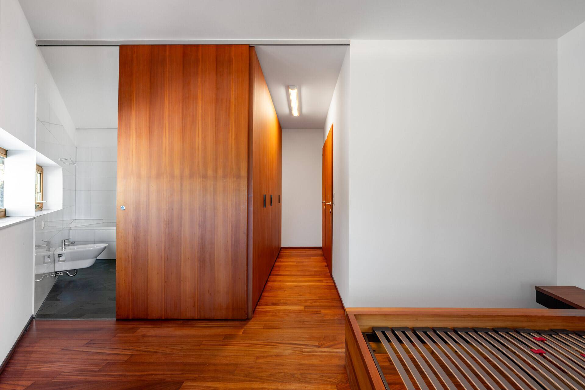 Schlafzimmer mit Holzboden, integrierten Holzschränken und Zugang zum Badezimmer.