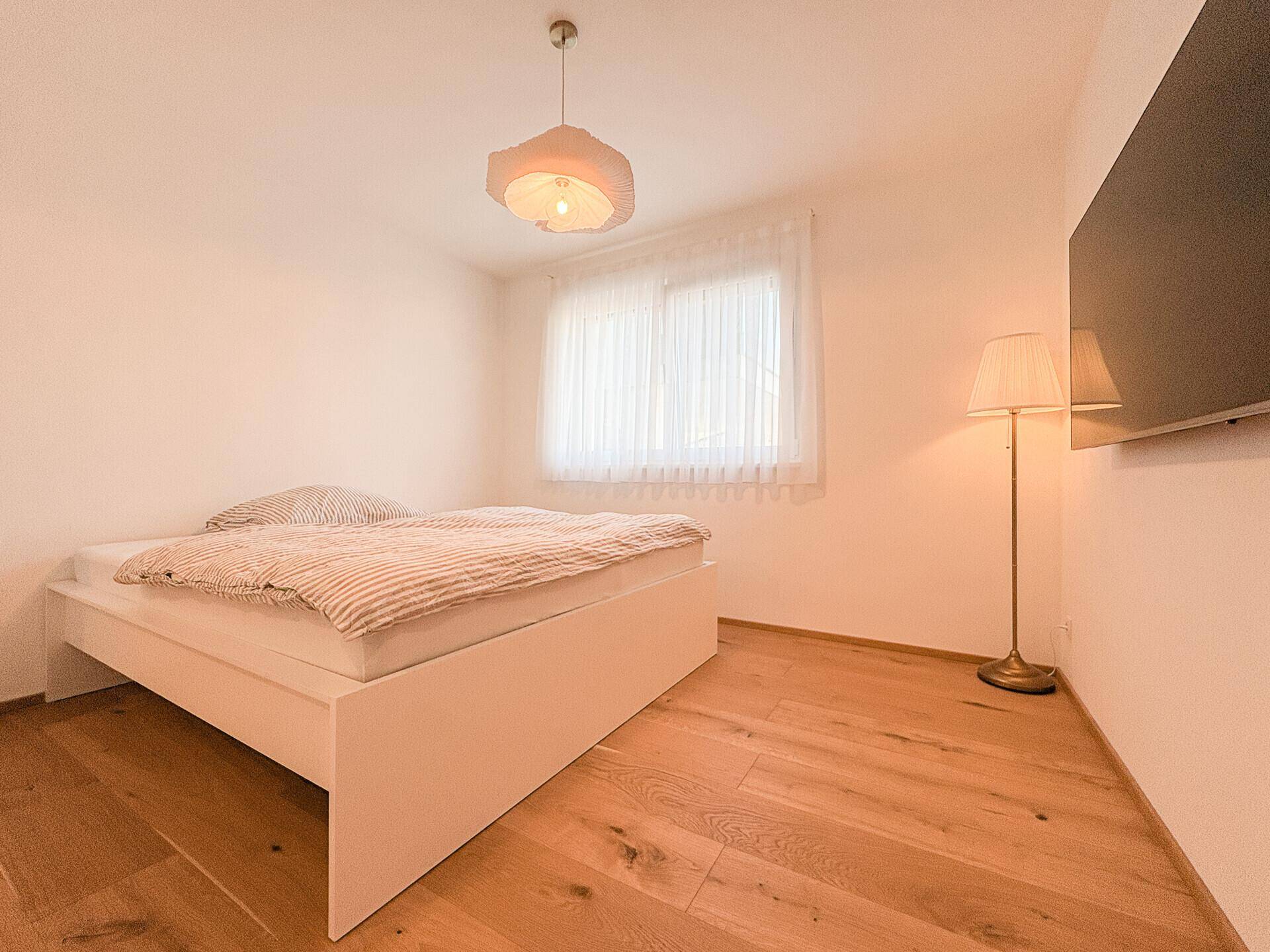 Ruhiges Schlafzimmer mit Holzboden, großem Fenster und indirekter Beleuchtung.