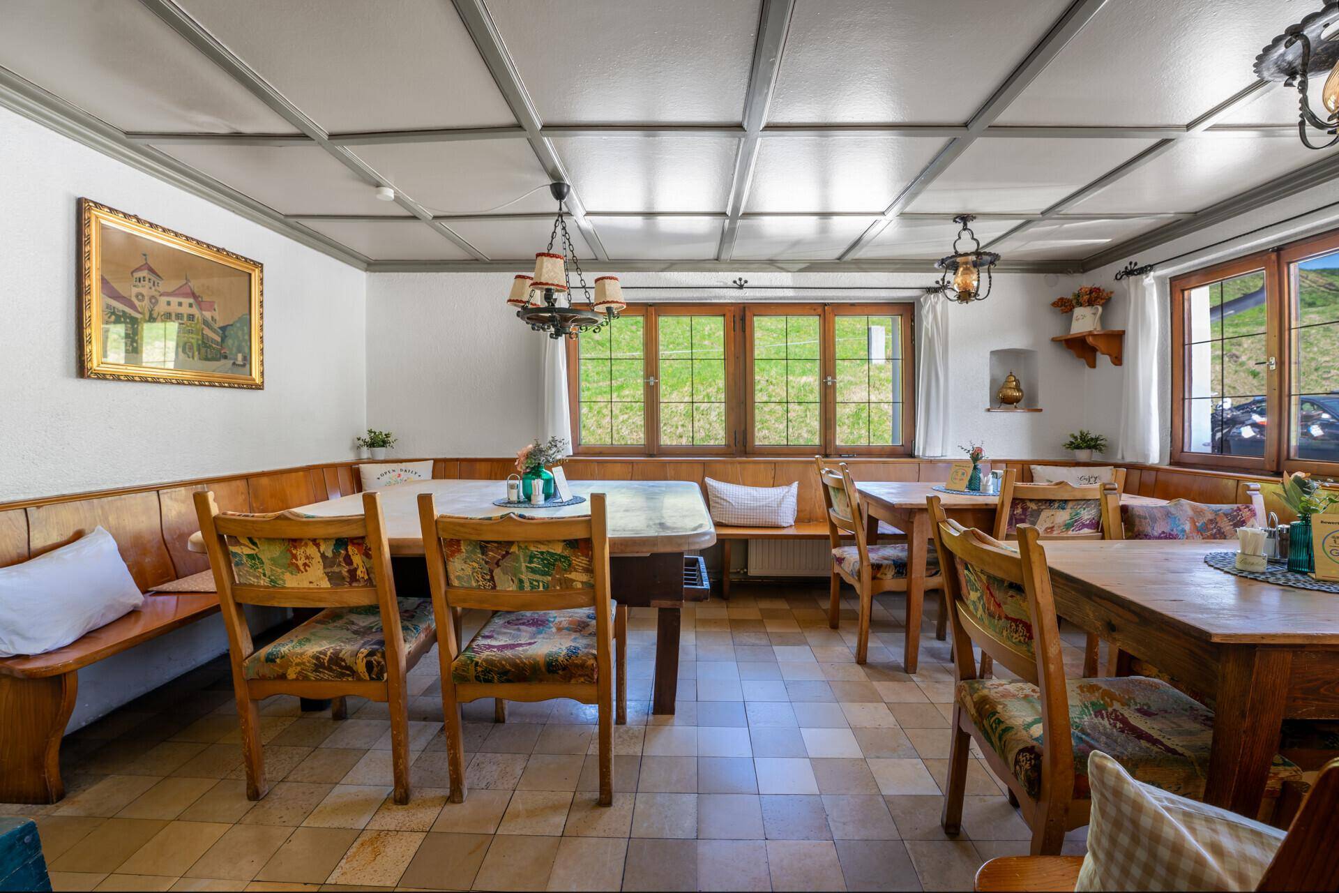Traditioneller Speisesaal mit Holzbänken und Tischen, karierten Kissen und Blick auf die grüne Landschaft.