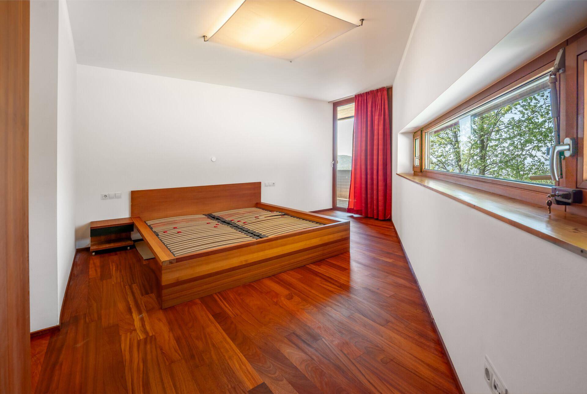 Helles Schlafzimmer mit Holzboden, großem Fenster und Zugang zu einem Balkon.
