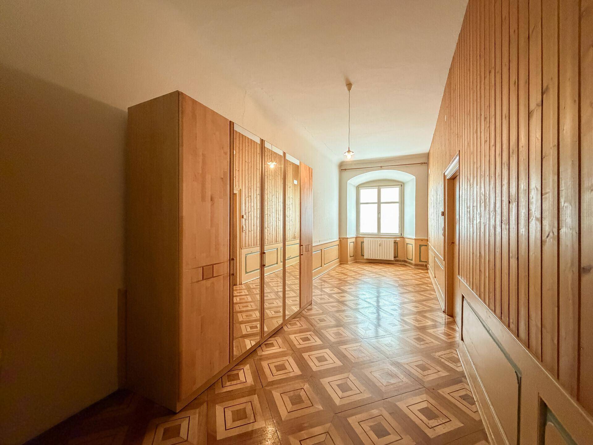 Langer Flur mit Holztäfelung, Parkettboden und großem Spiegelschrank.