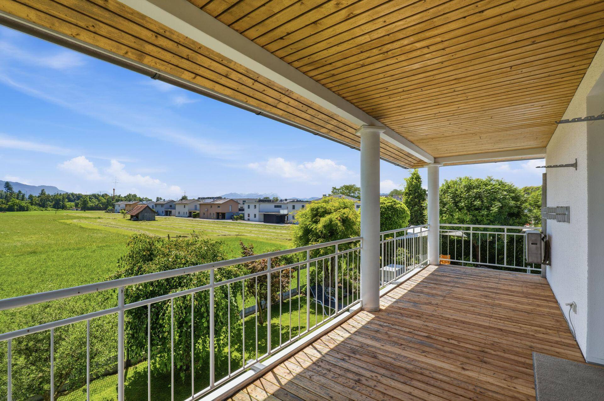 Großer Holzbalkon mit Metallgeländer und weitem Blick über die grüne Landschaft.