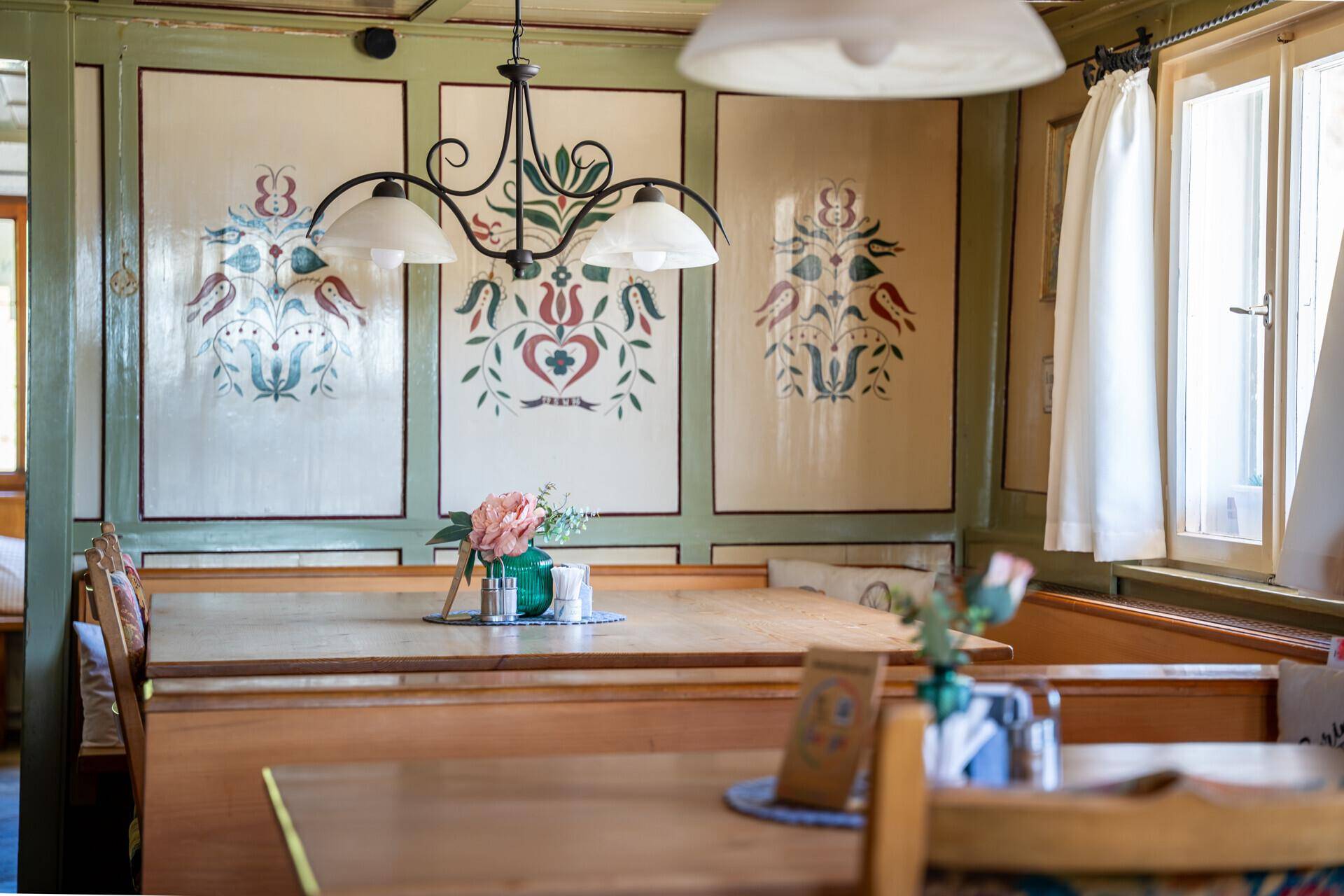 Detailansicht eines traditionellen Speisesaals mit handgemalten Wanddekorationen und rustikalen Holzmöbeln.
