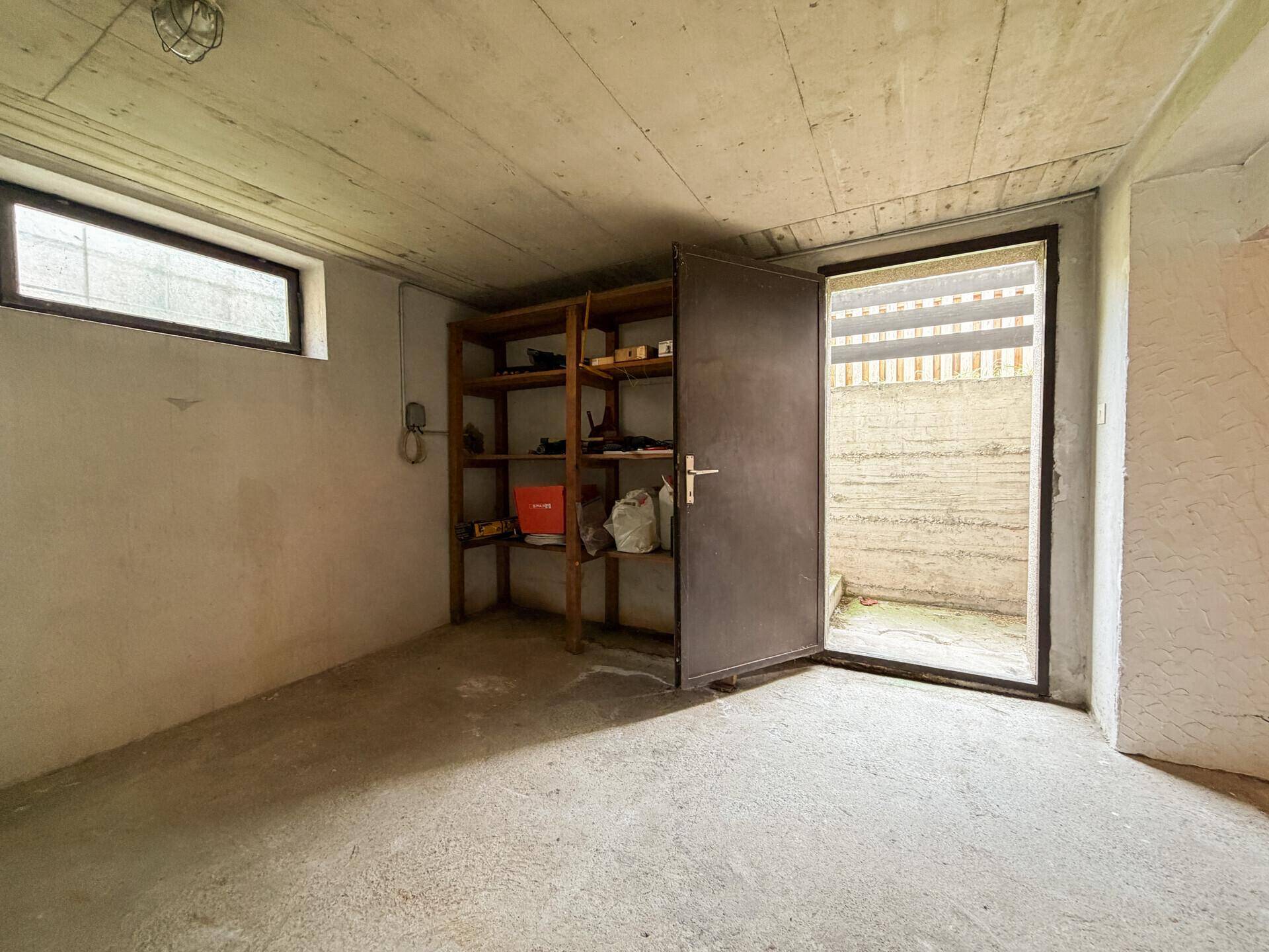 Kellerraum mit Betonboden, Regalen und direktem Zugang nach draußen, ideal für Lagerung.