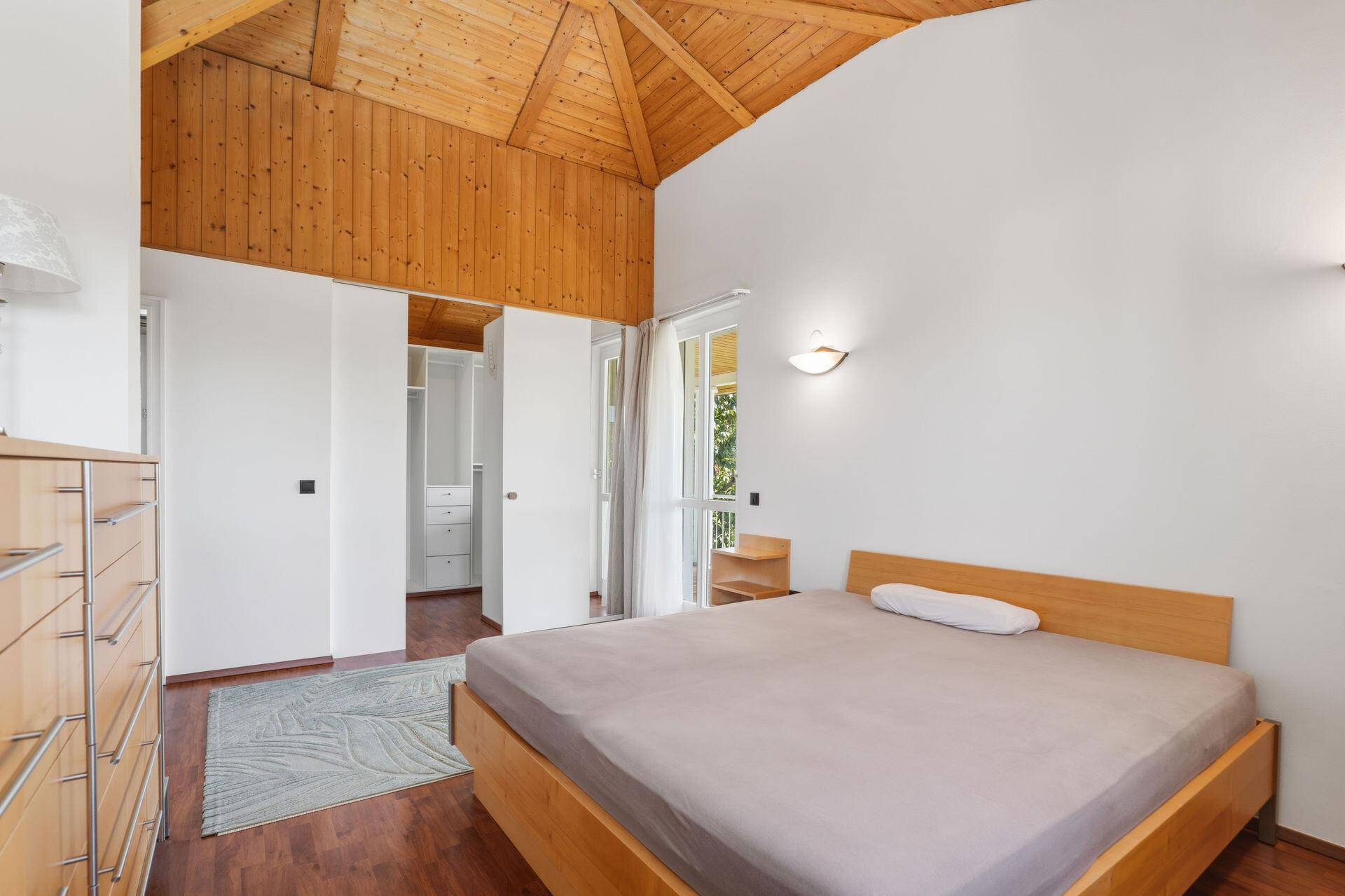 Gemütliches Schlafzimmer mit Holzbalkendecke, Holzboden und Zugang zu einem begehbaren Kleiderschrank.