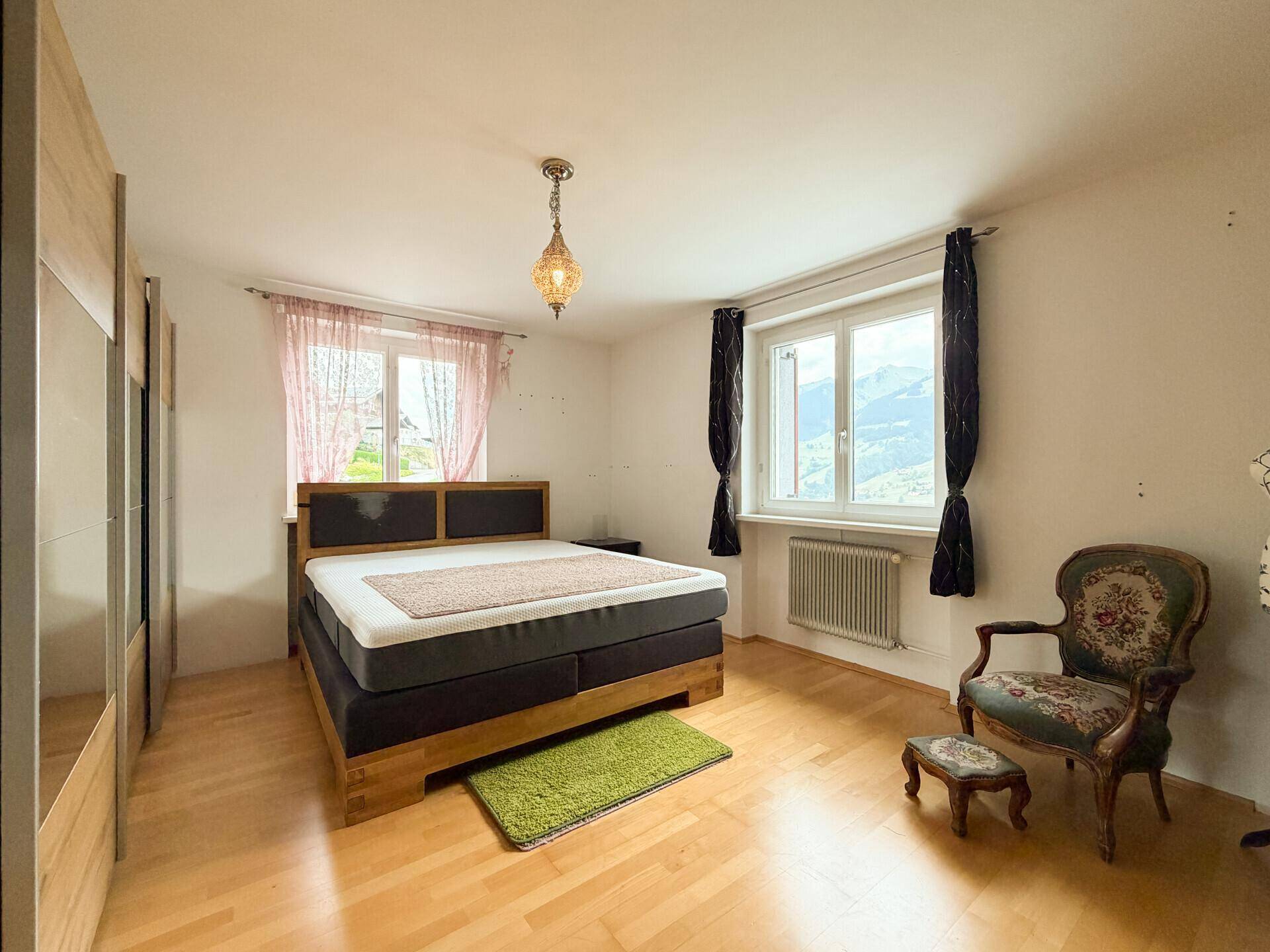 Gemütliches Schlafzimmer mit Holzboden, Doppelbett und einem Sessel mit Bergblick.
