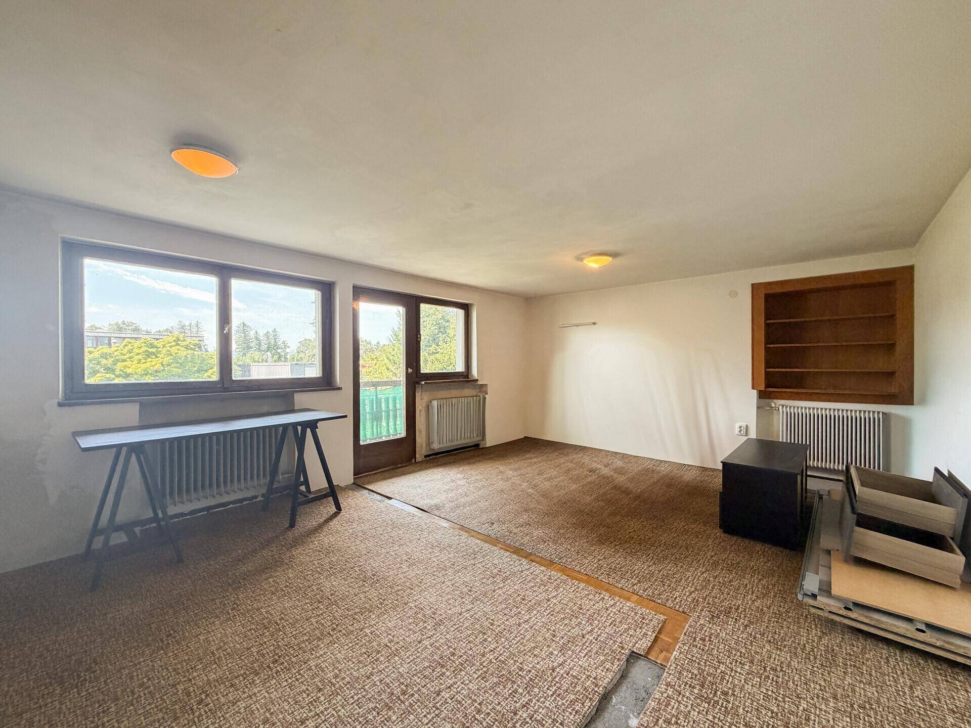 Helles Wohnzimmer mit Teppichboden und Zugang zu einem Balkon, bietet viel Tageslicht.