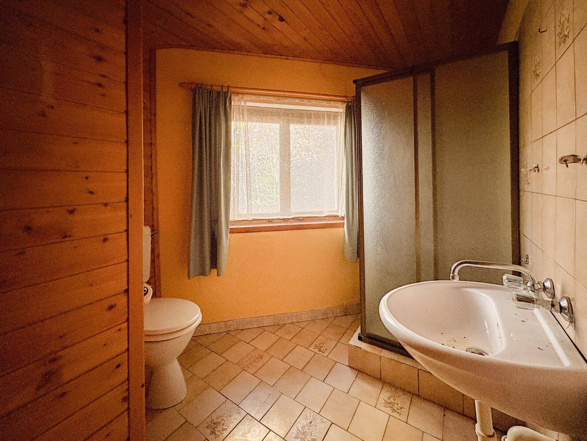 Badezimmer mit Fliesenboden, Duschkabine, WC und Fenster.