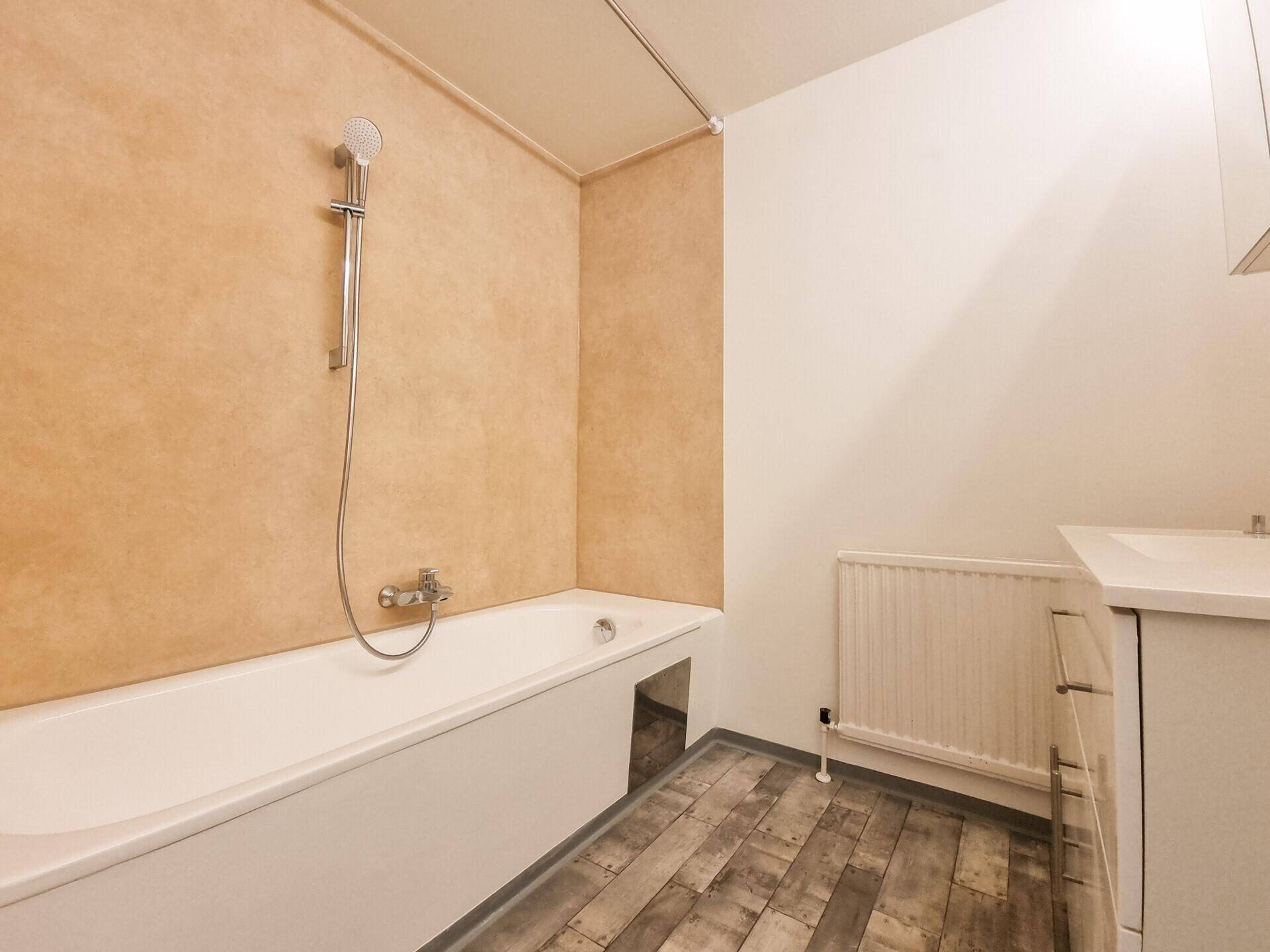 Badezimmer mit Badewanne, Duscharmatur und modernem Vinylboden in Holzoptik.