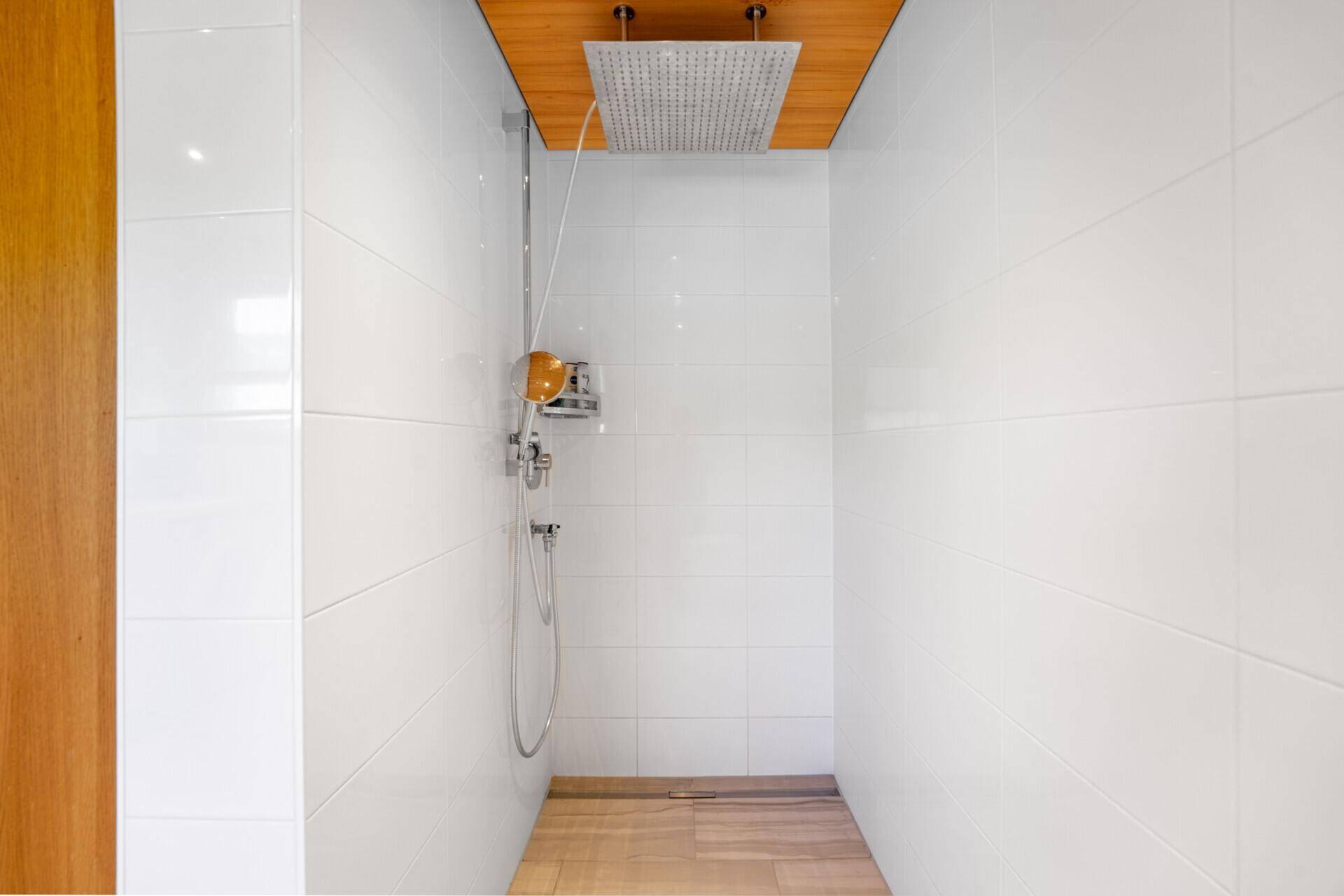 Moderne Duschkabine mit weißen Fliesenwänden und großem Regenduschkopf, mit Holzoptik-Fliesenboden.