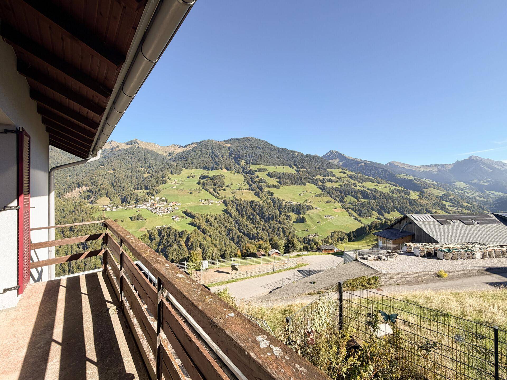 Balkon mit Holzgeländer und weitem Blick auf die umliegende Berglandschaft und das Tal.