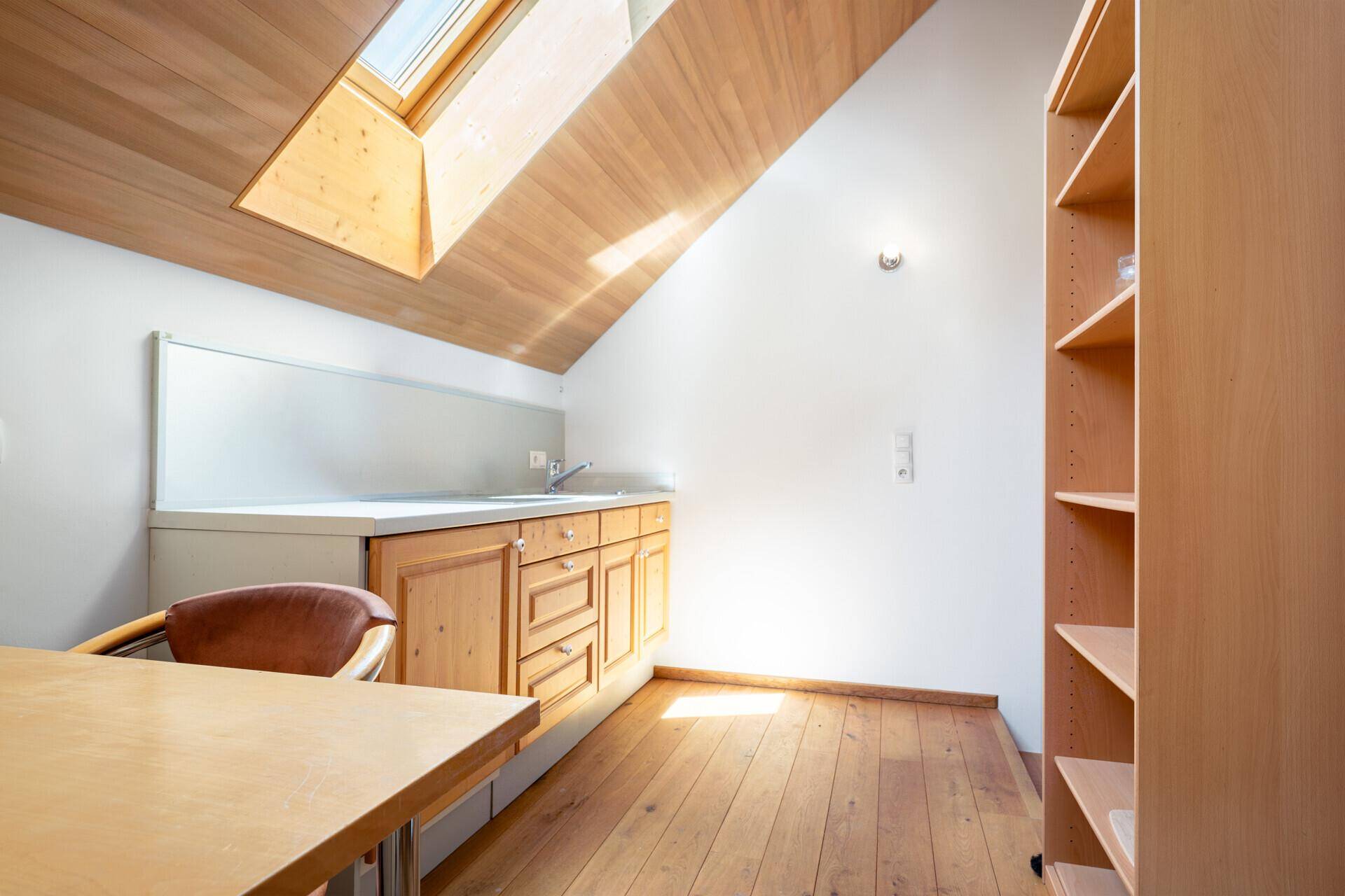 Gemütliche Küchenzeile im Dachgeschoss mit Holzbalkendecke, Dachfenster und viel natürlichem Licht.