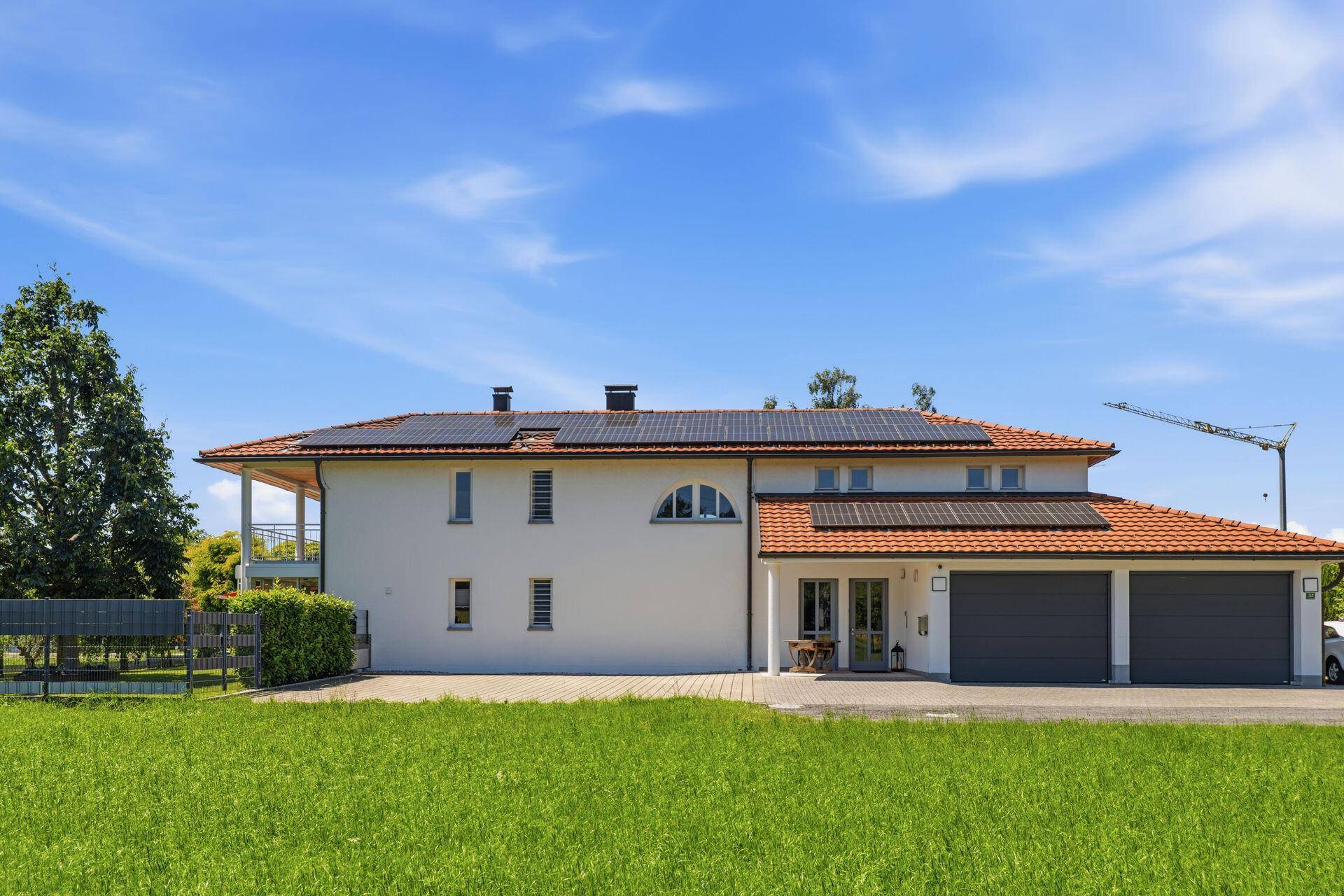 Modernes Einfamilienhaus mit Photovoltaikanlage auf dem Dach und gepflegtem Vorgarten unter blauem Himmel.