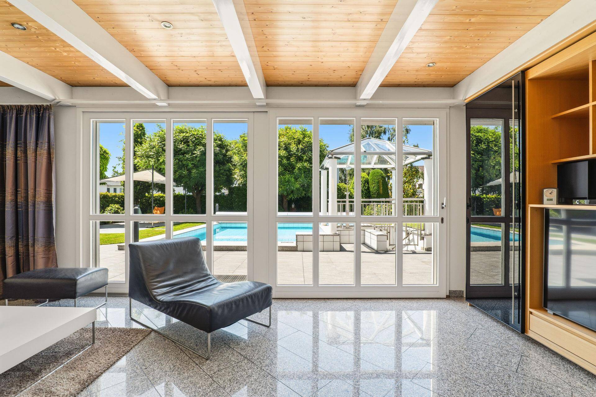 Helles Wohnzimmer mit großen Fenstern und direktem Blick auf den Poolbereich.