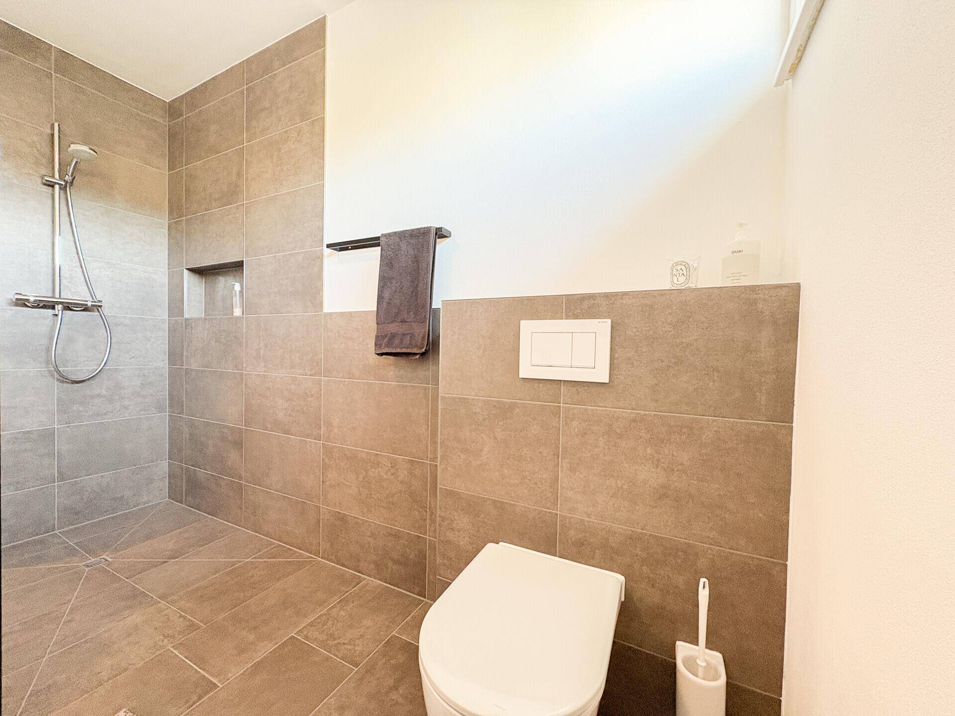 Geräumige ebenerdige Dusche und modernes Wand-WC in einem hellen Badezimmer.