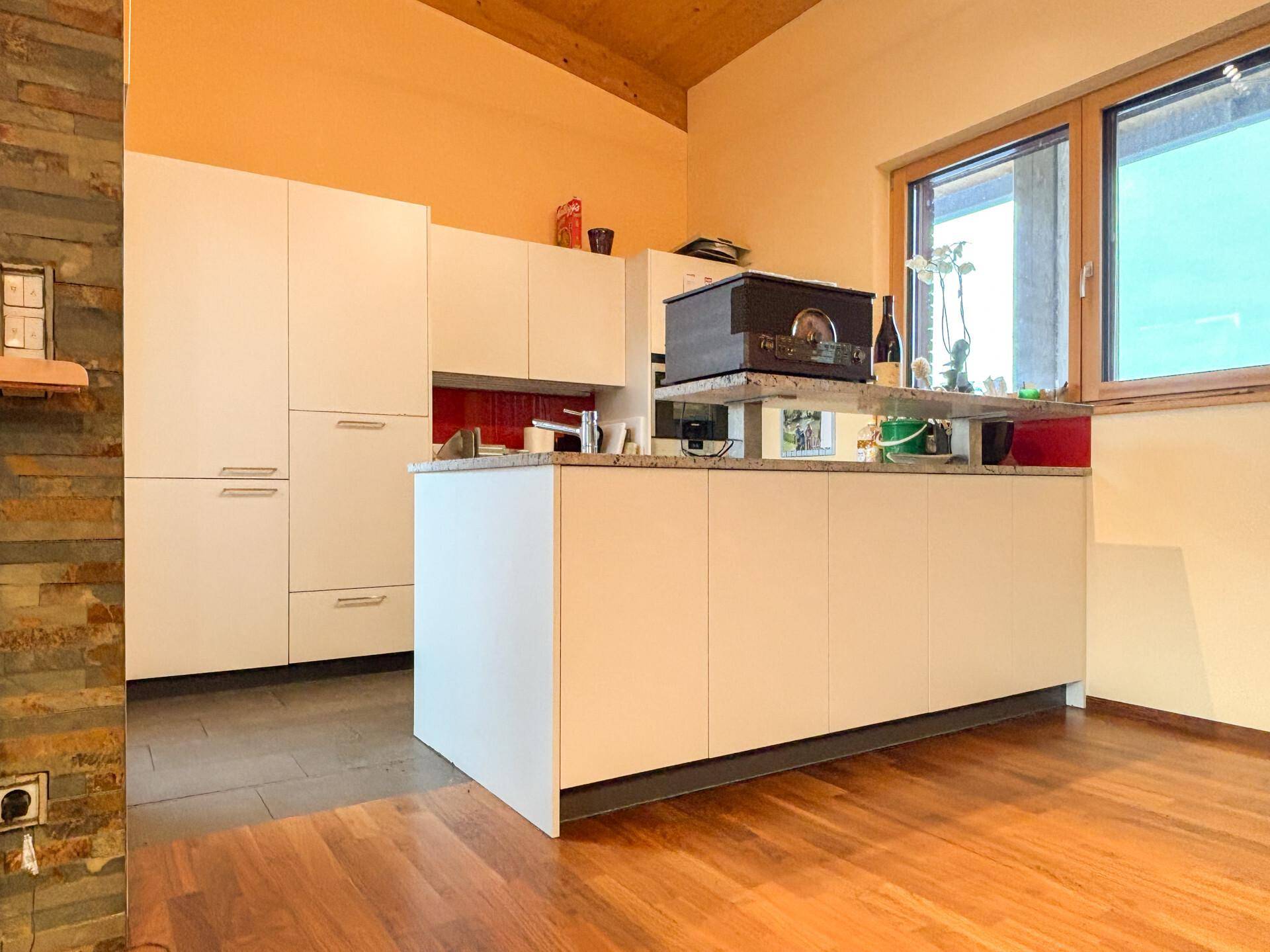 Moderne weiße Küche mit Granitarbeitsplatte, Holzdecke und Fenster für natürliches Licht.