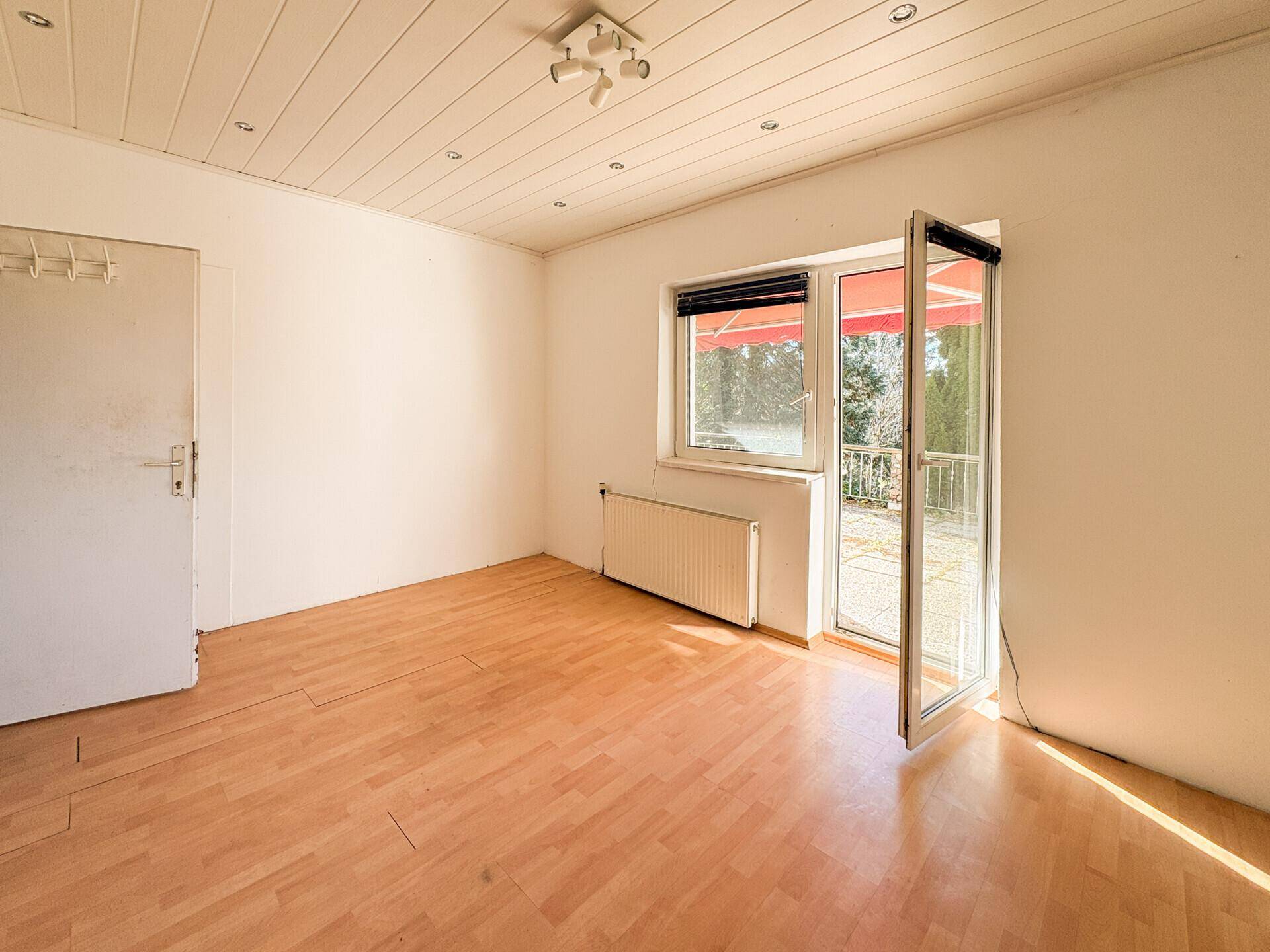 Helles Zimmer mit Holzfußboden und großer Terrassentür, die viel Sonnenlicht hereinlässt.