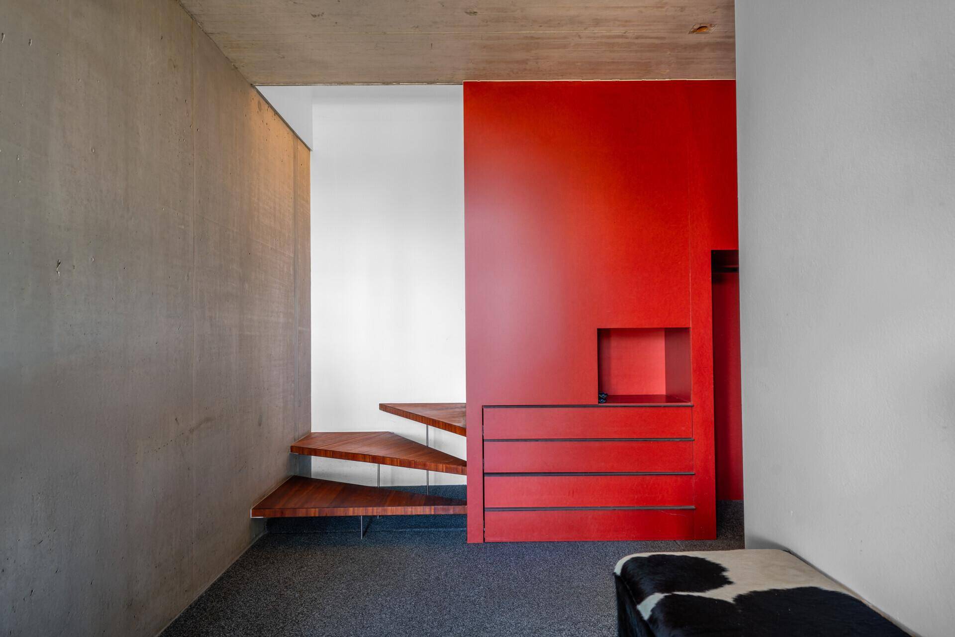 Flur mit roter Akzentwand, integrierten Schubladen und schwebender Holztreppe.
