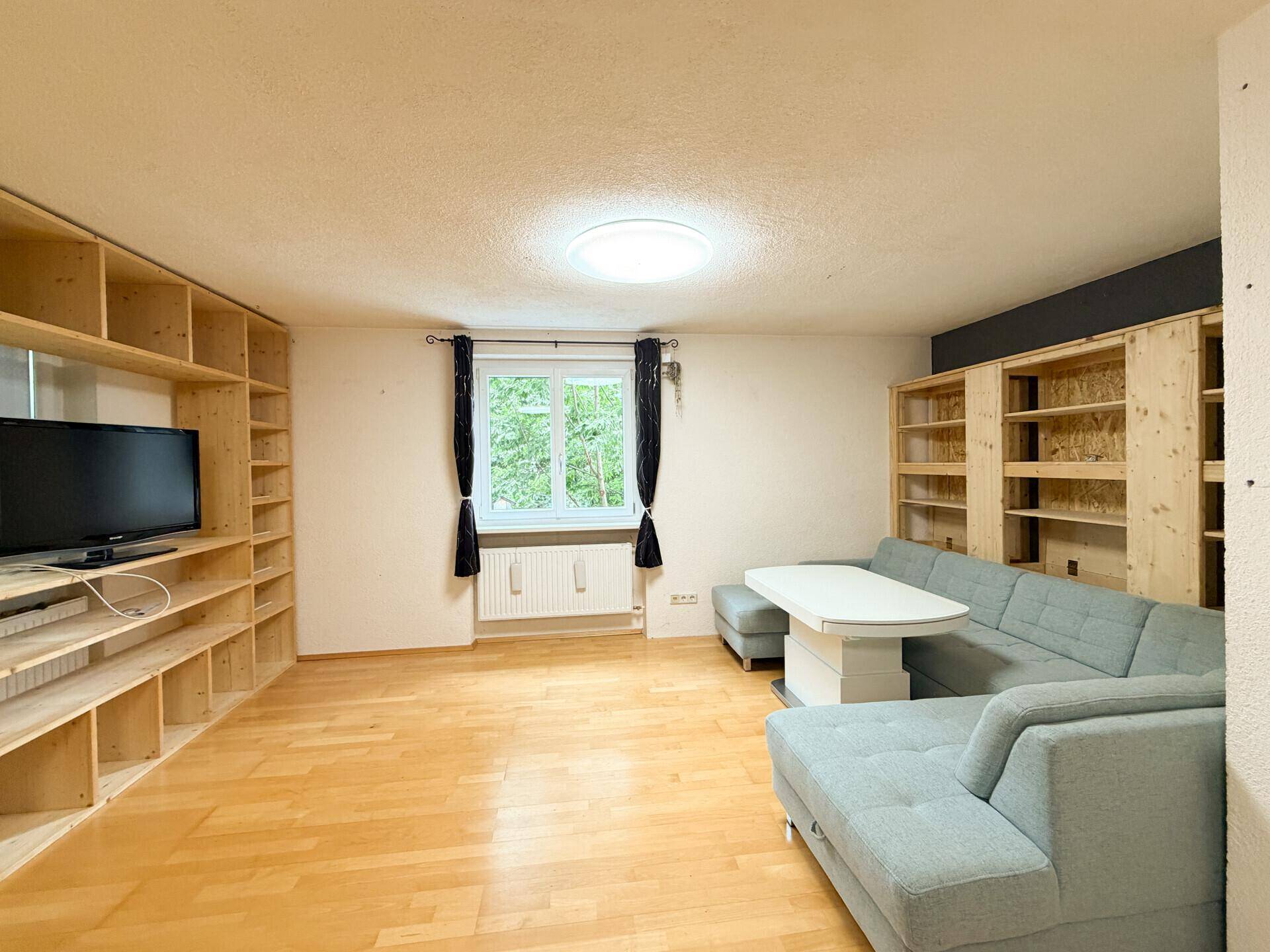 Geräumiges Wohnzimmer mit Holzboden, integrierten Regalen und einem bequemen Sofa.