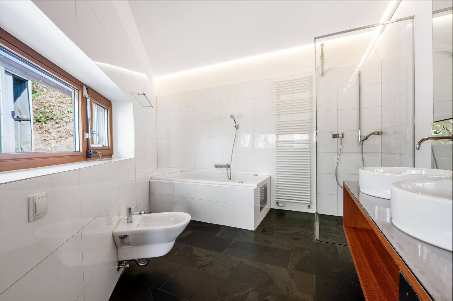 Modernes Badezimmer mit Badewanne, Bidet, Dusche und dunklen Fliesen.