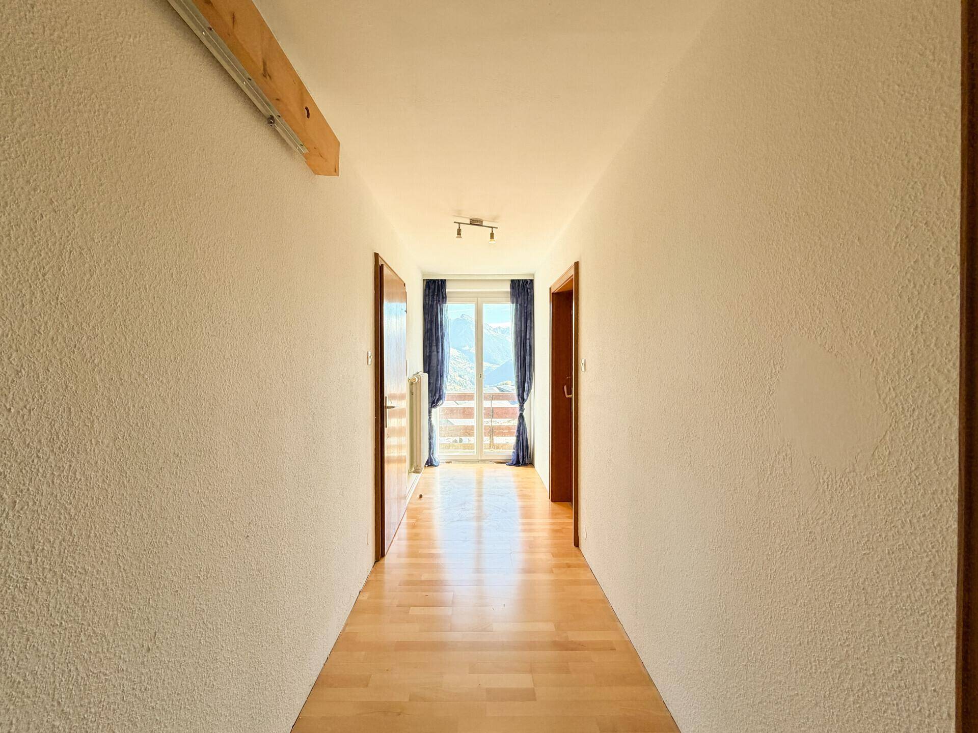 Heller Flur mit Holzparkettboden, der zu einem Raum mit Bergblick und Balkonzugang führt.