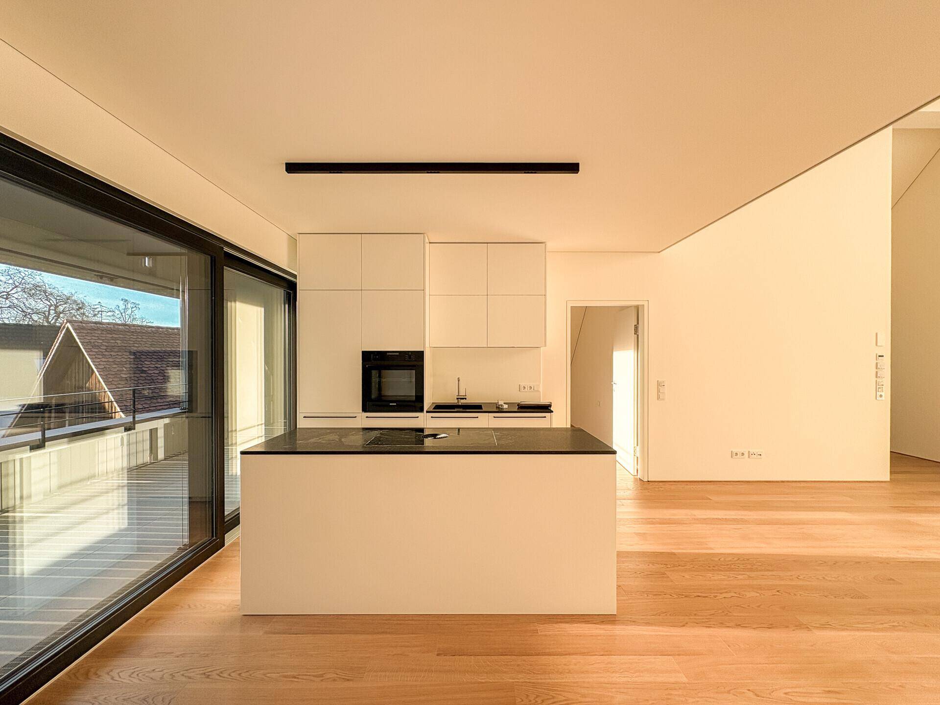 Minimalistische weiße Küche mit dunkler Arbeitsplatte auf der Kücheninsel und integriertem Backofen.