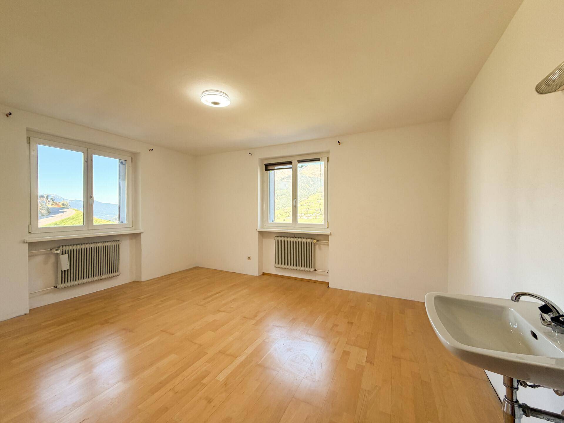 Heller Raum mit Holzparkettboden und zwei Fenstern, ausgestattet mit einem Waschbecken in der Ecke.