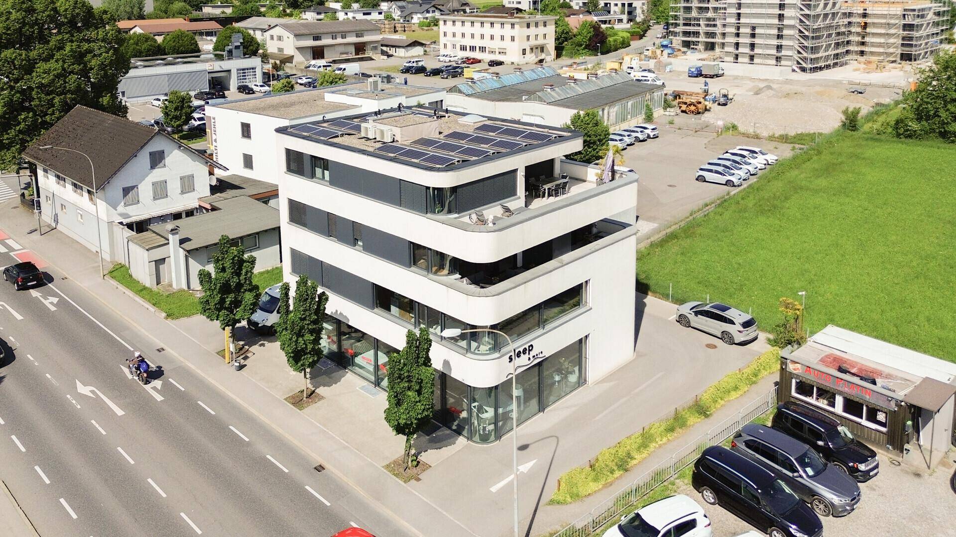 Luftaufnahme des modernen Gebäudes mit Photovoltaikanlage auf dem Flachdach und umliegender Natur.