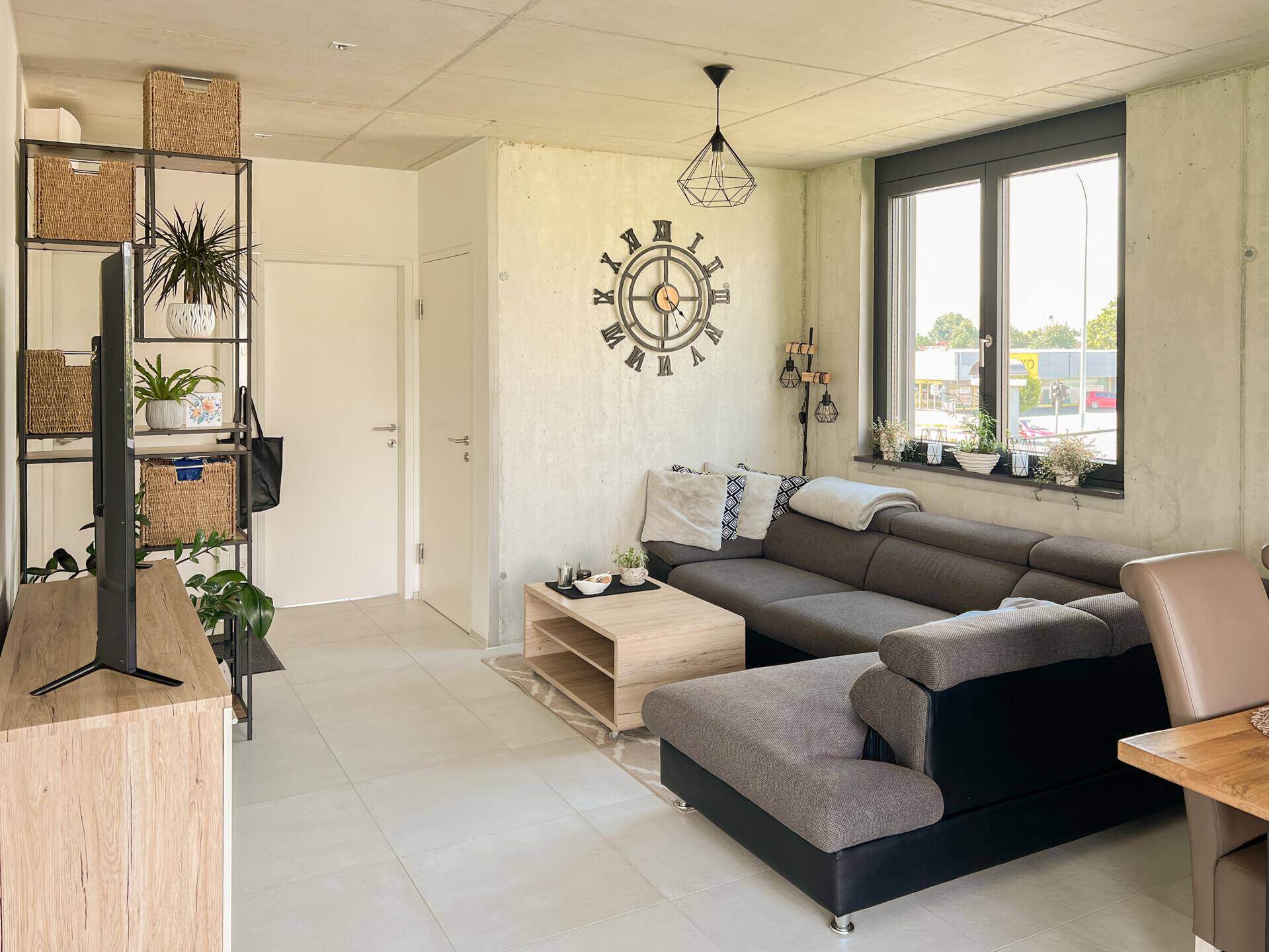 Gemütliches Wohnzimmer mit großem Ecksofa, Fliesenboden und großen Fenstern für viel Licht.