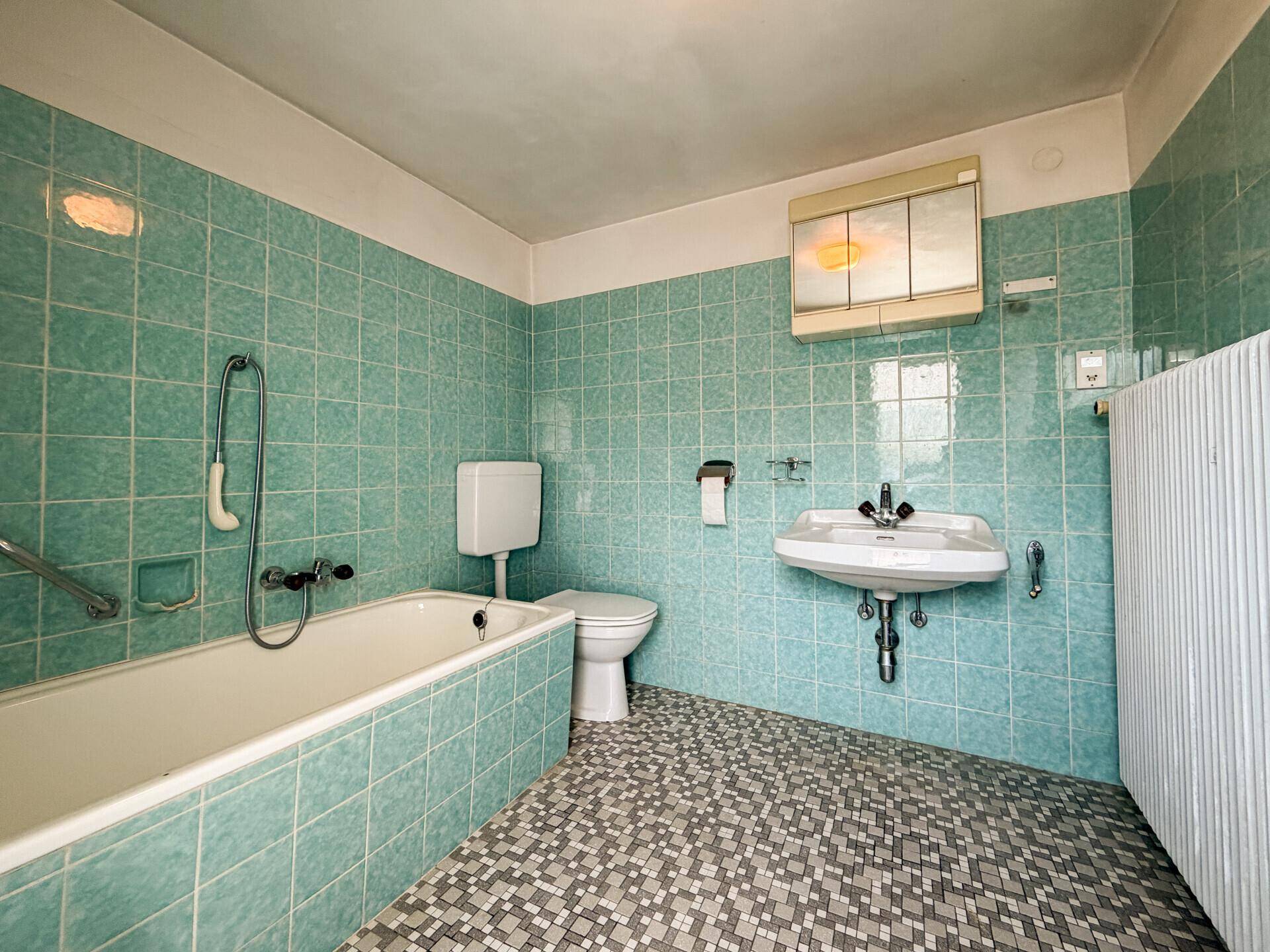 Badezimmer im Stil der 80er Jahre mit türkisfarbenen Fliesen, Badewanne und Waschbecken.