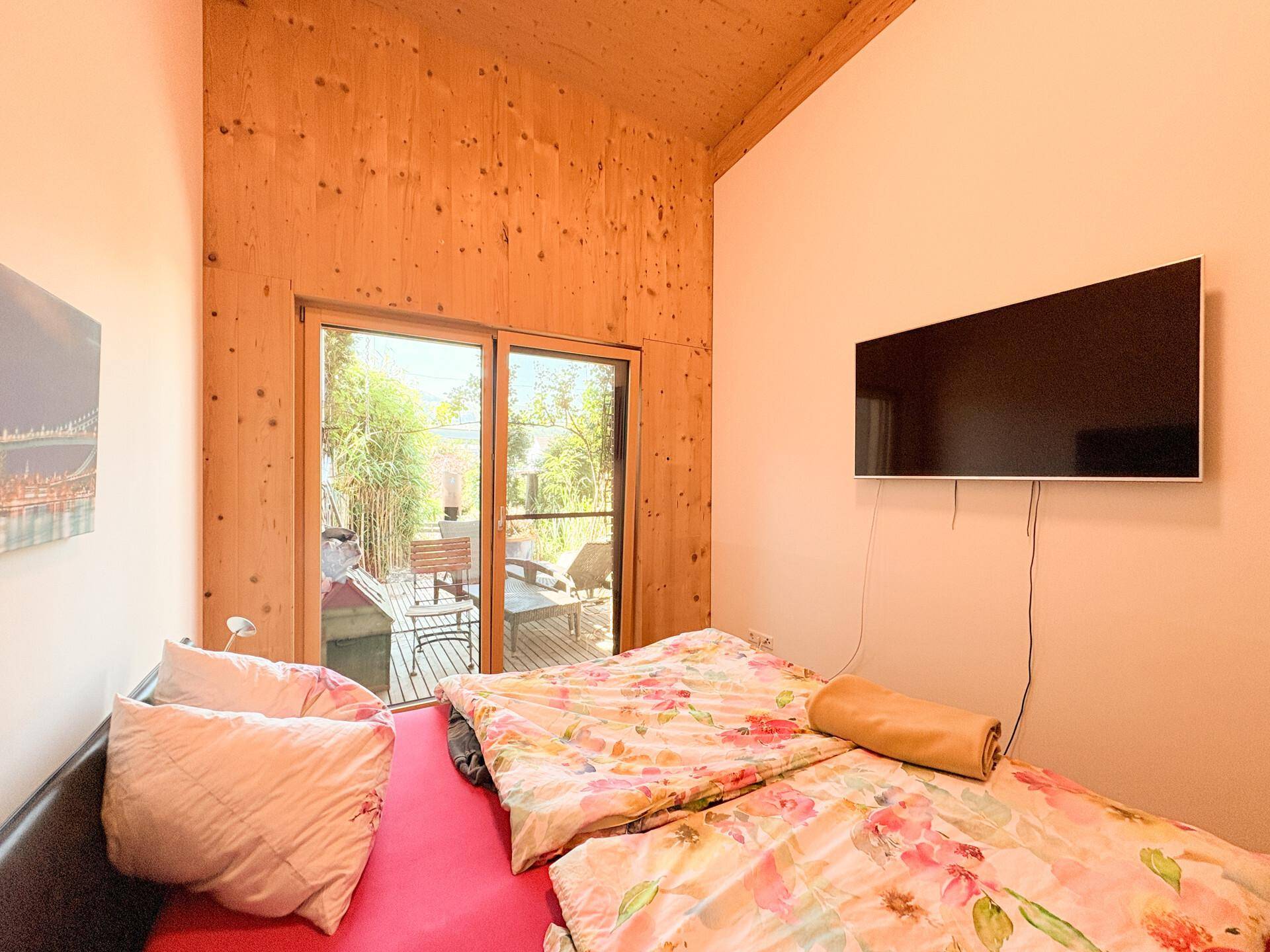 Gemütliches Schlafzimmer mit Holzwänden, Fernseher und direktem Zugang zur Terrasse.