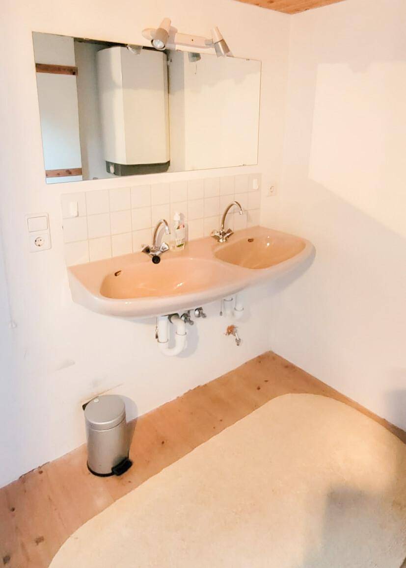 Badezimmer mit Doppelwaschbecken in Pastellfarbe, Spiegel und weiß gefliestem Spritzschutz.