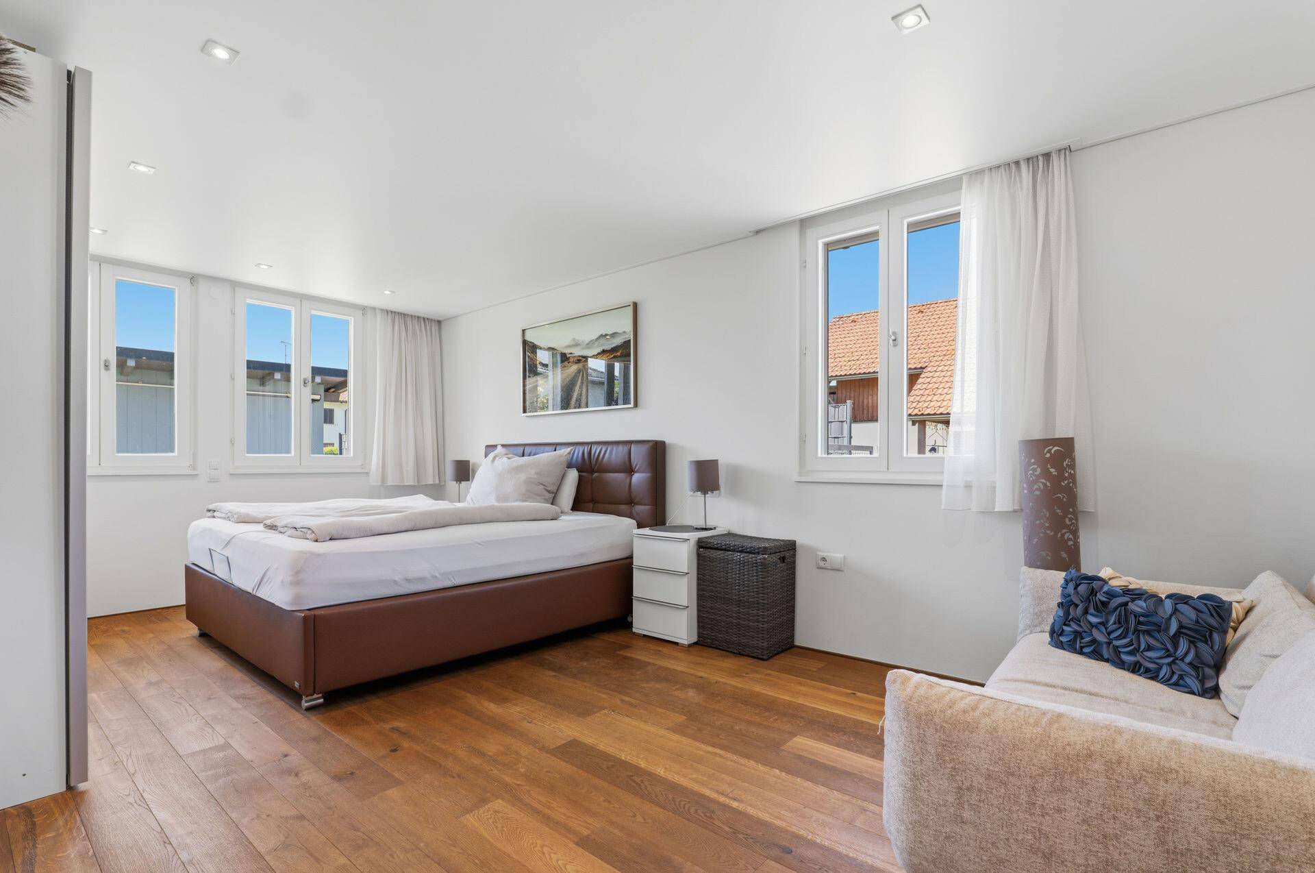 Geräumiges Schlafzimmer mit Doppelbett, Holzboden und mehreren Fenstern.