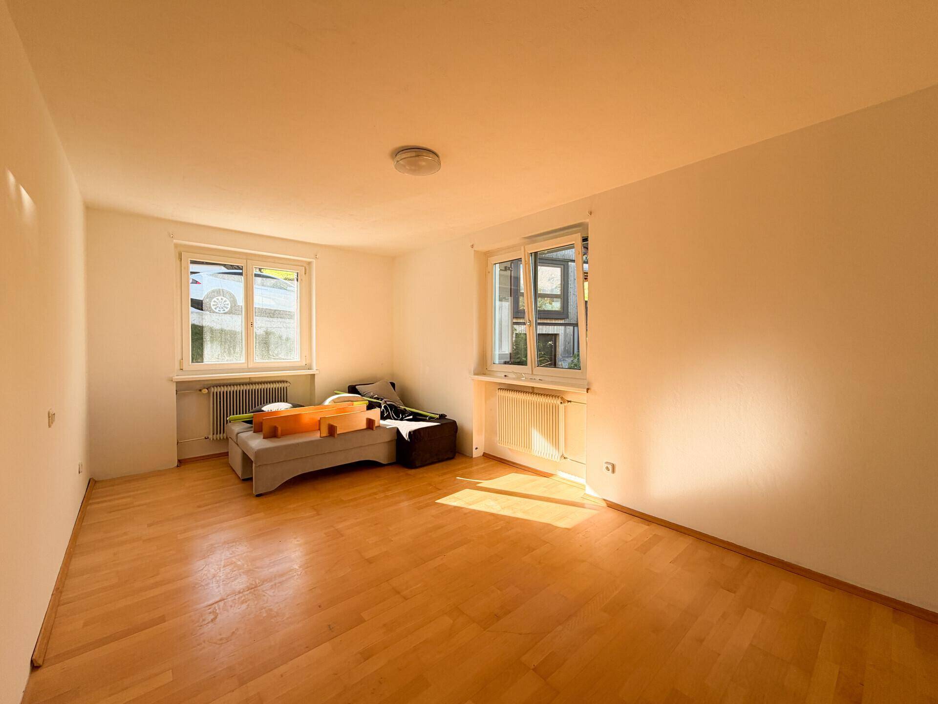 Lichtdurchfluteter Raum mit Holzparkettboden und zwei Fenstern, bietet eine helle und freundliche Atmosphäre.