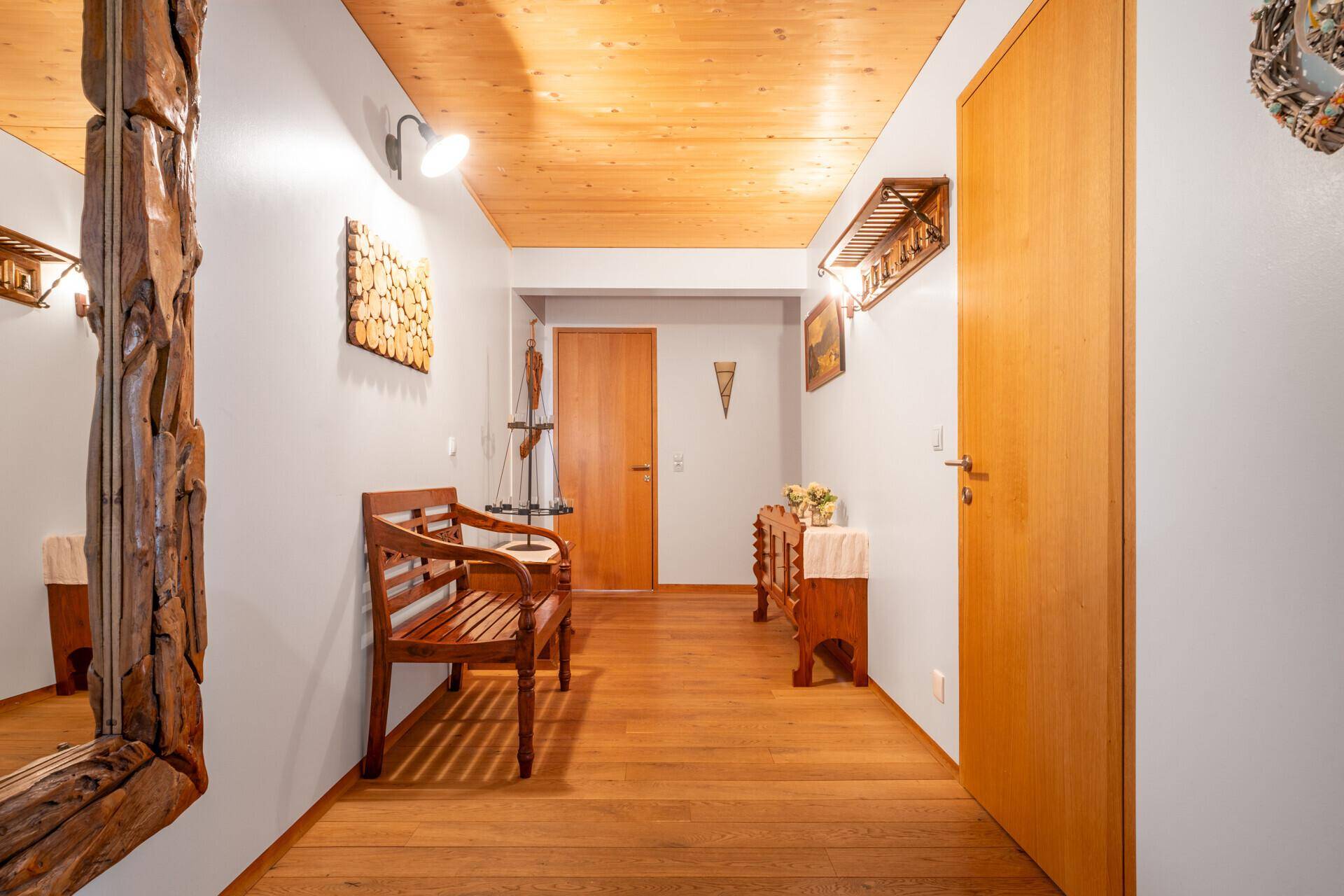 Heller Flur mit Holzdielenboden, hellgrauen Wänden und einer Holzlamellendecke, inklusive Holzbank und Spiegel.