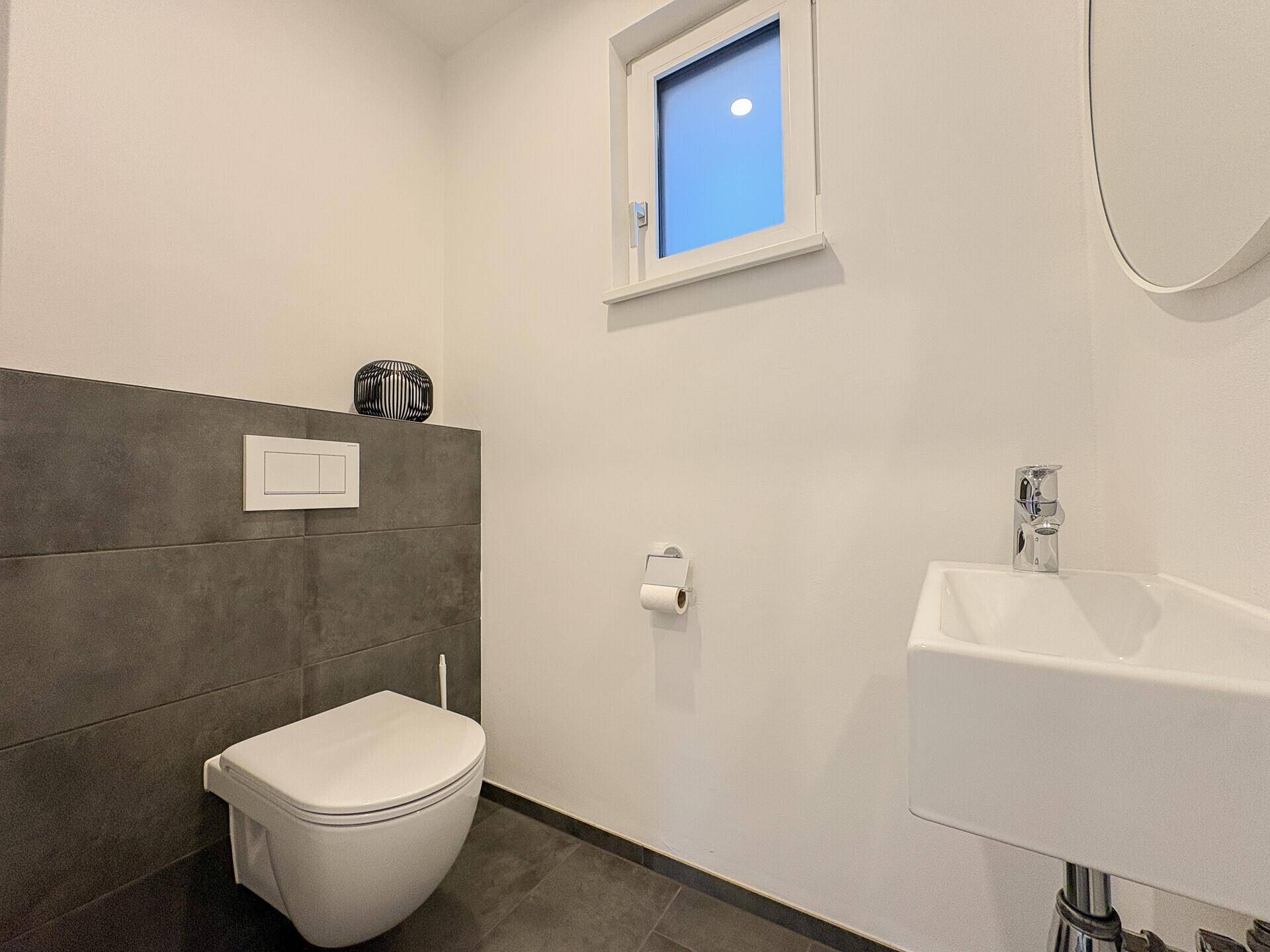 Modernes Gäste-WC mit Wand-WC, kleinem Waschbecken und Fenster für Tageslicht.