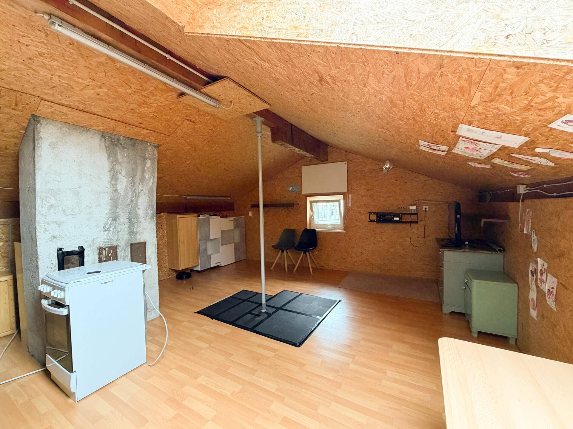 Ausgebauter Dachboden mit Holzverkleidung, Schrägen und einem kleinen Fenster.