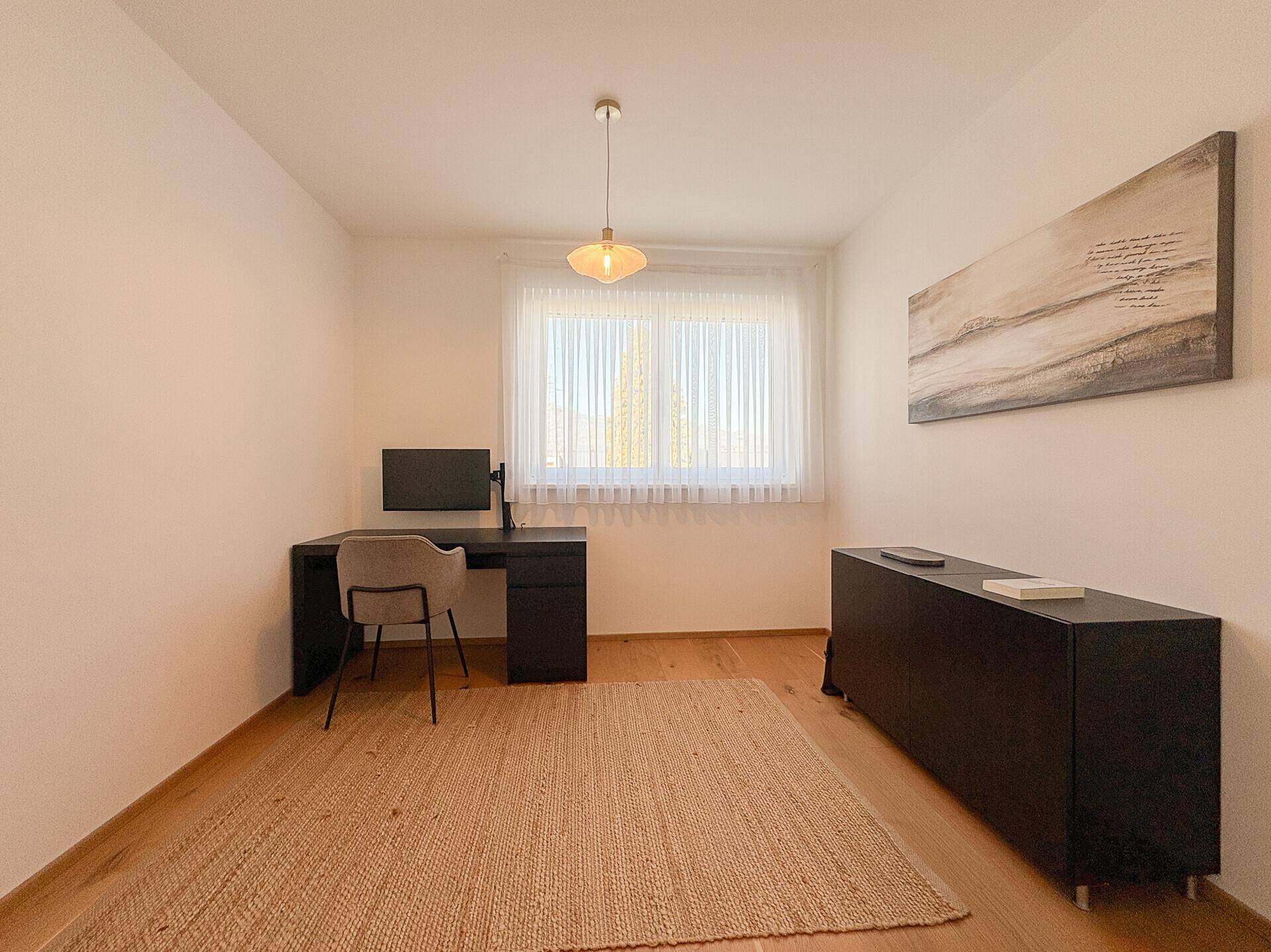 Funktionales Arbeitszimmer mit Holzboden, Schreibtisch und großem Fenster.