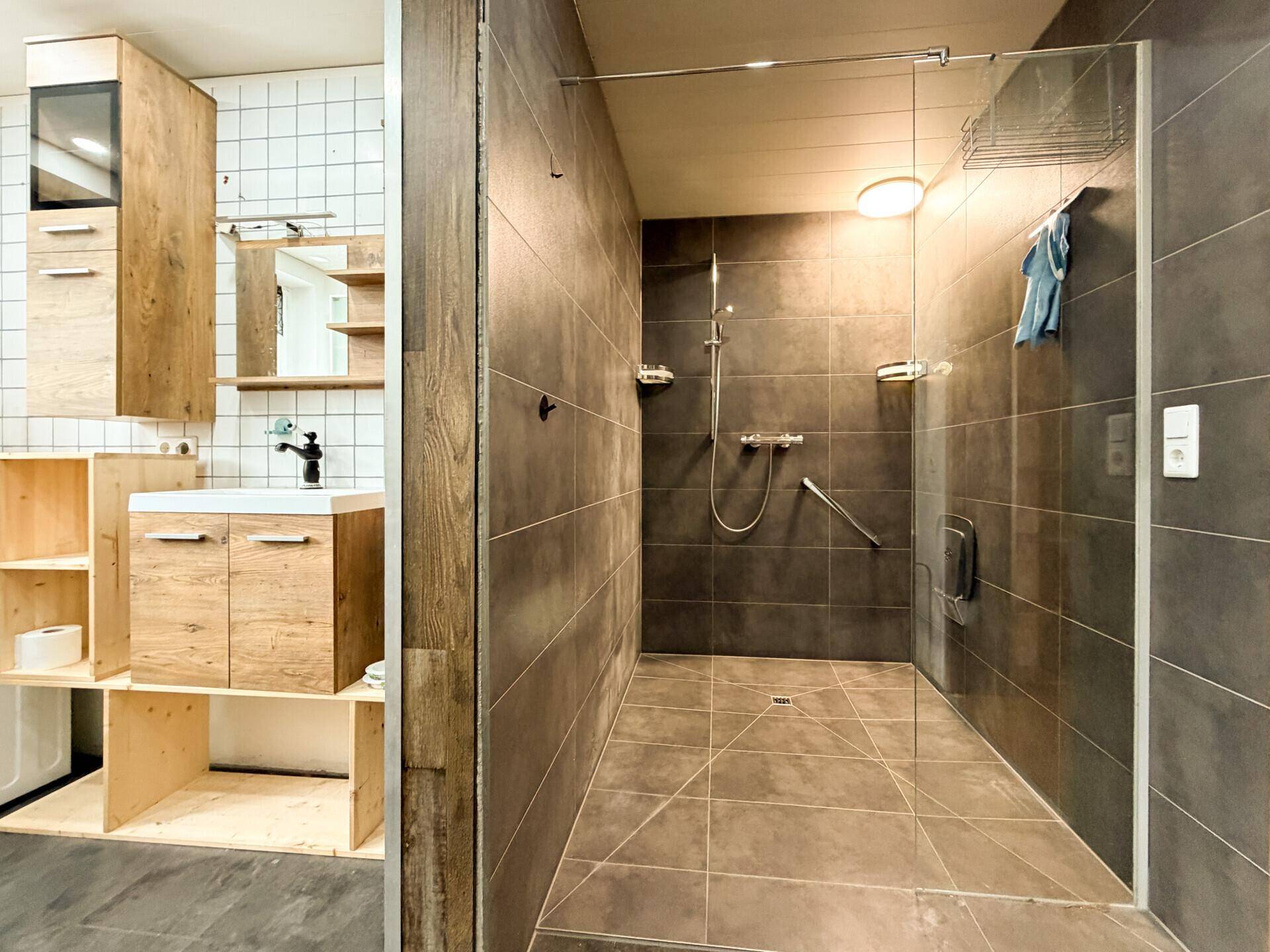 Geräumige ebenerdige Dusche und Waschtisch mit Holzunterschrank im modernen Badezimmer.