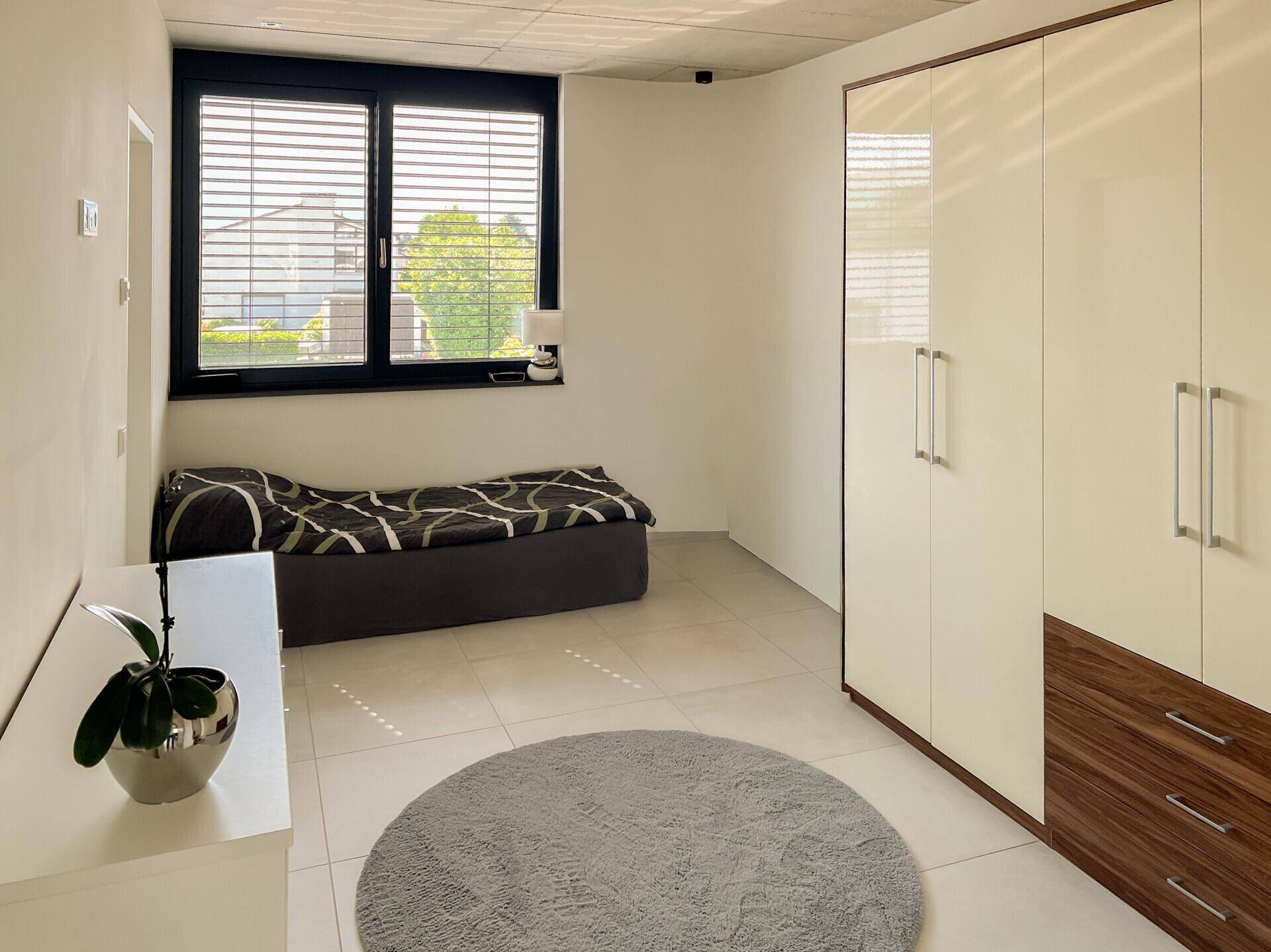 Schlafzimmer mit großem Kleiderschrank, Fliesenboden und Fenster mit Blick nach draußen.