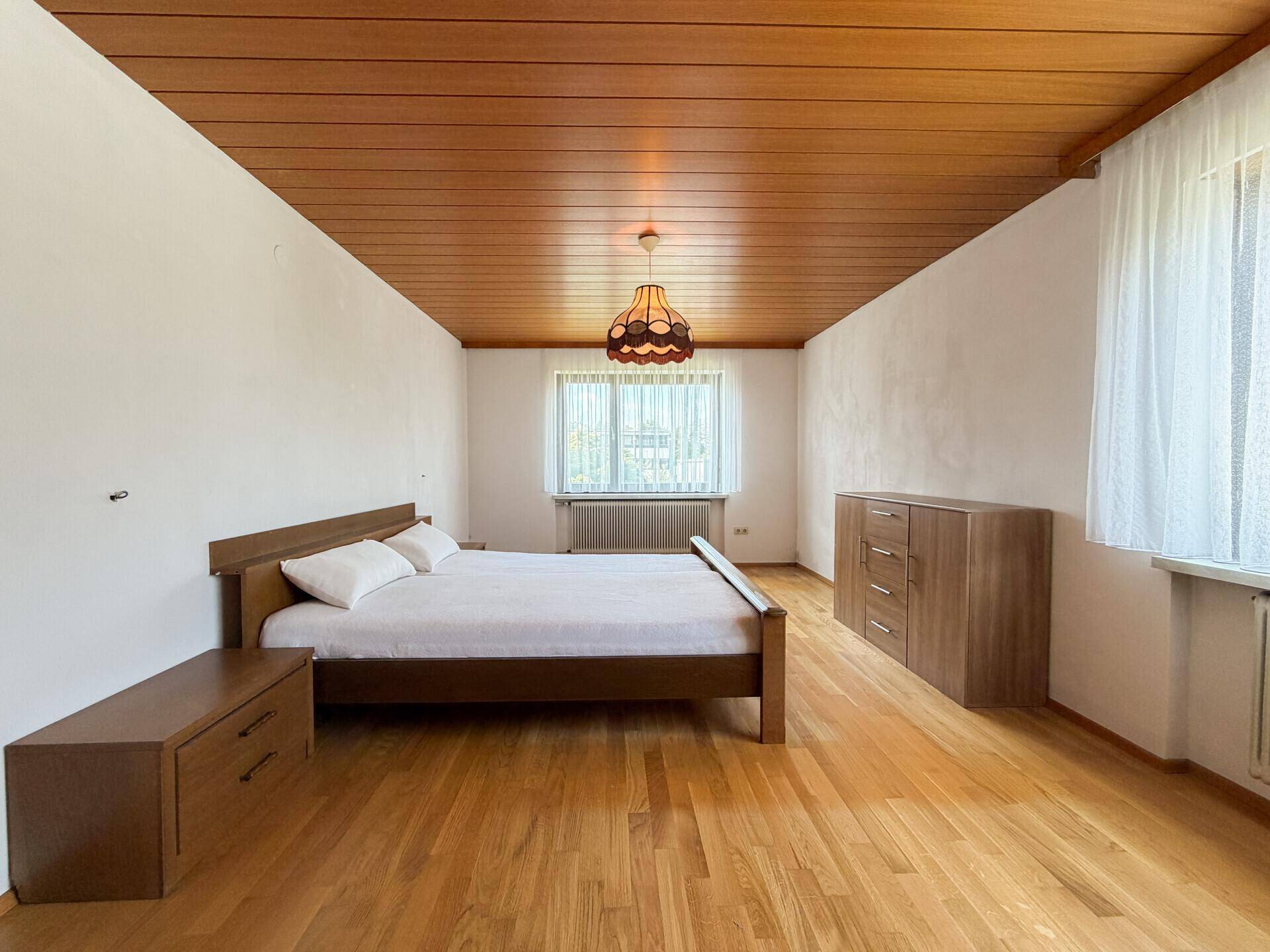 Geräumiges Schlafzimmer mit Holzboden, Holzdecke und einem großen Bett in hellem Holzton.