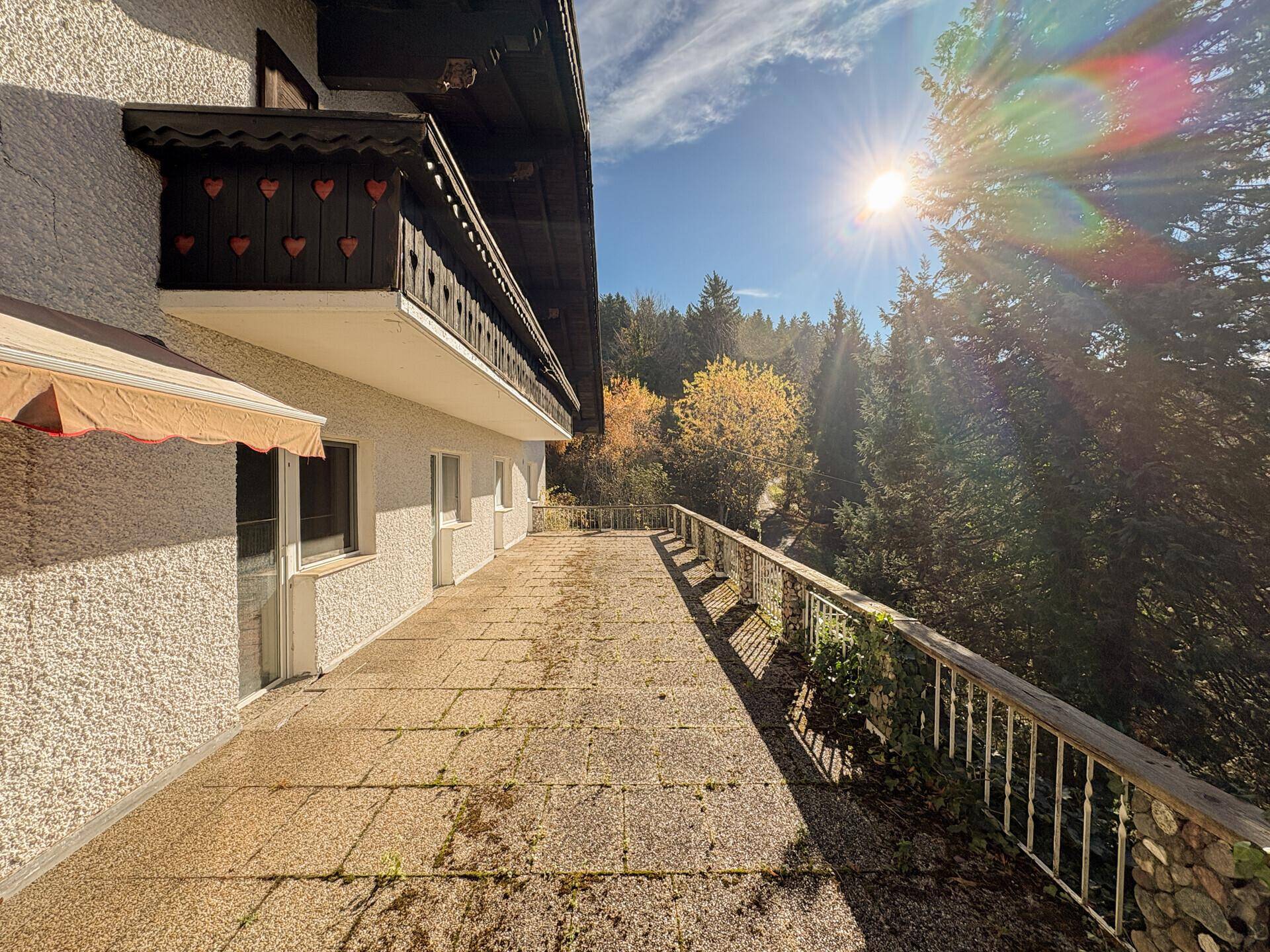 Große, sonnige Terrasse mit Fliesenboden und Holzzaun, umgeben von Bäumen.