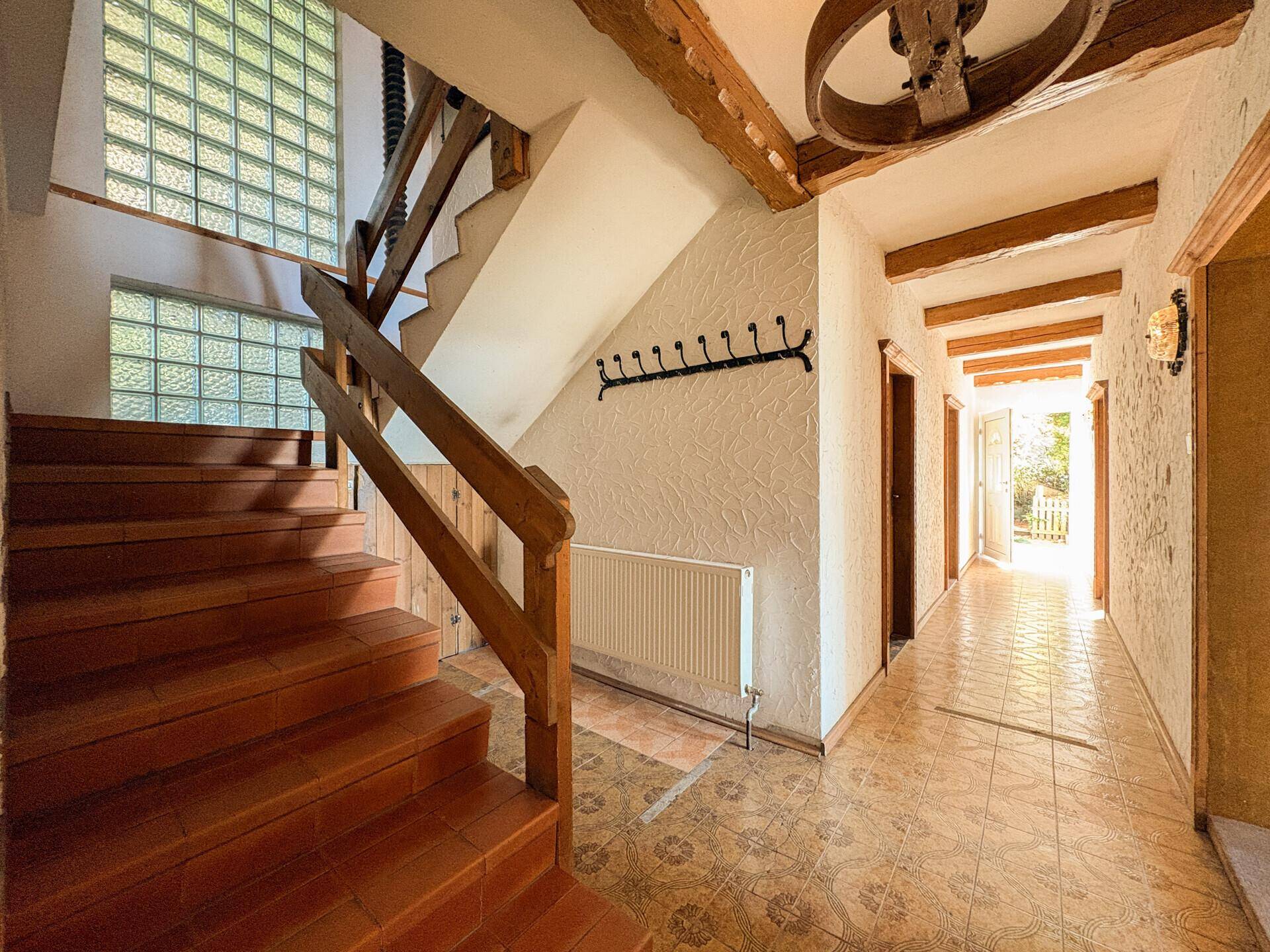 Geräumiger Flur mit Holztreppe, Fliesenboden und Glasbausteinen für natürliches Licht.
