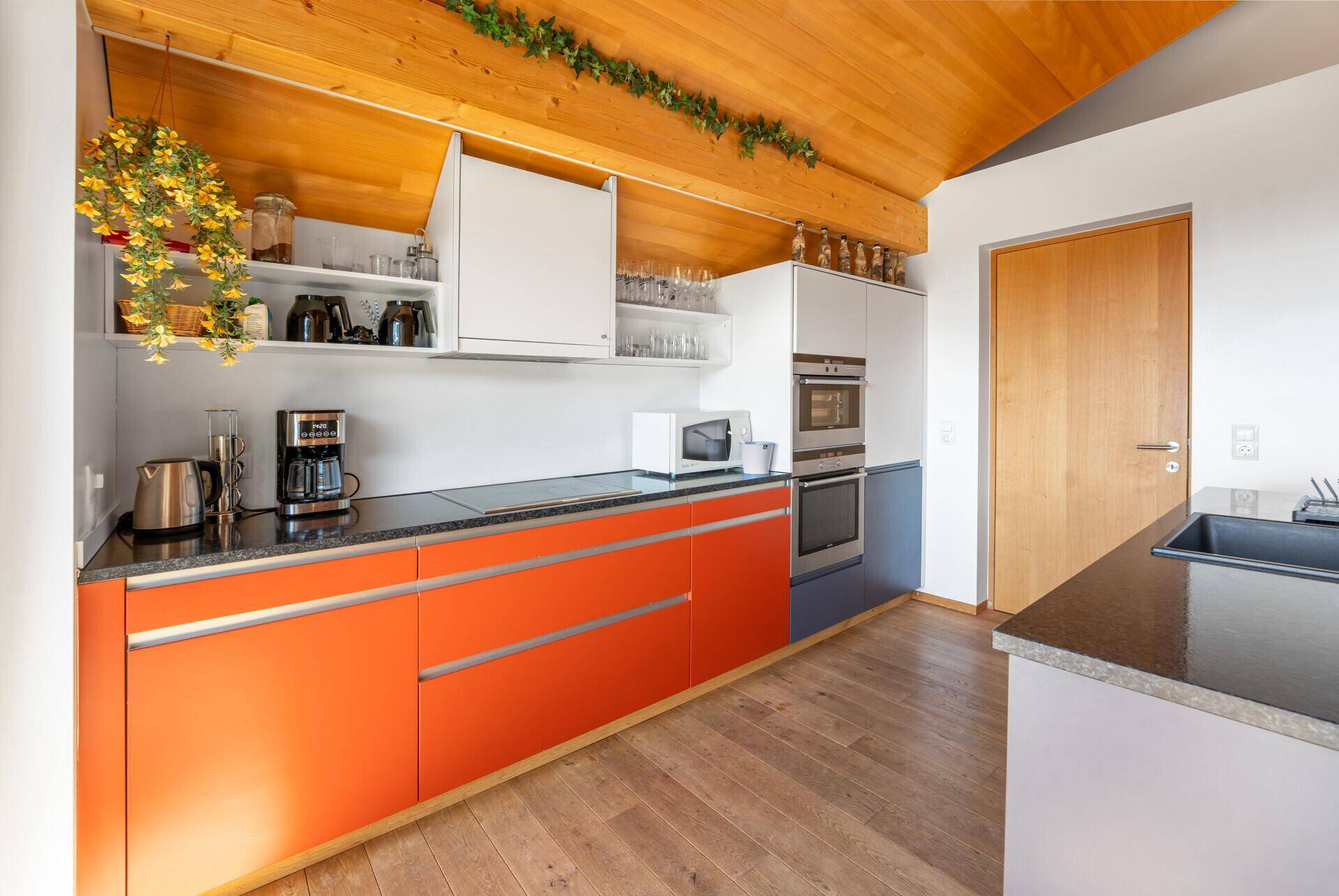 Moderne Küche mit orangefarbenen und weißen Schränken, Einbaugeräten und einer Holzdecke.