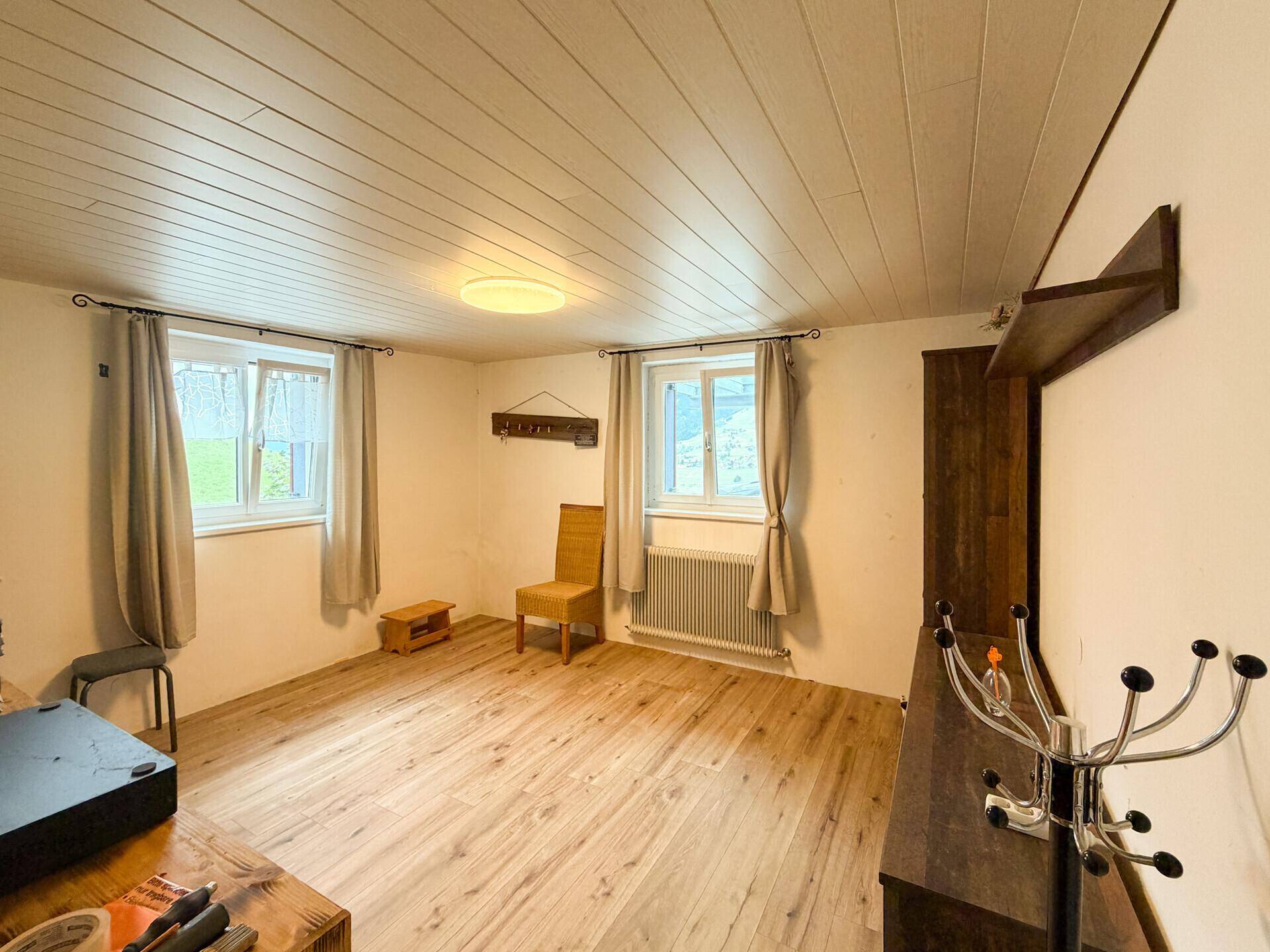 Leeres Zimmer mit Holzboden, weißer Holzdecke und zwei Fenstern für viel Licht.