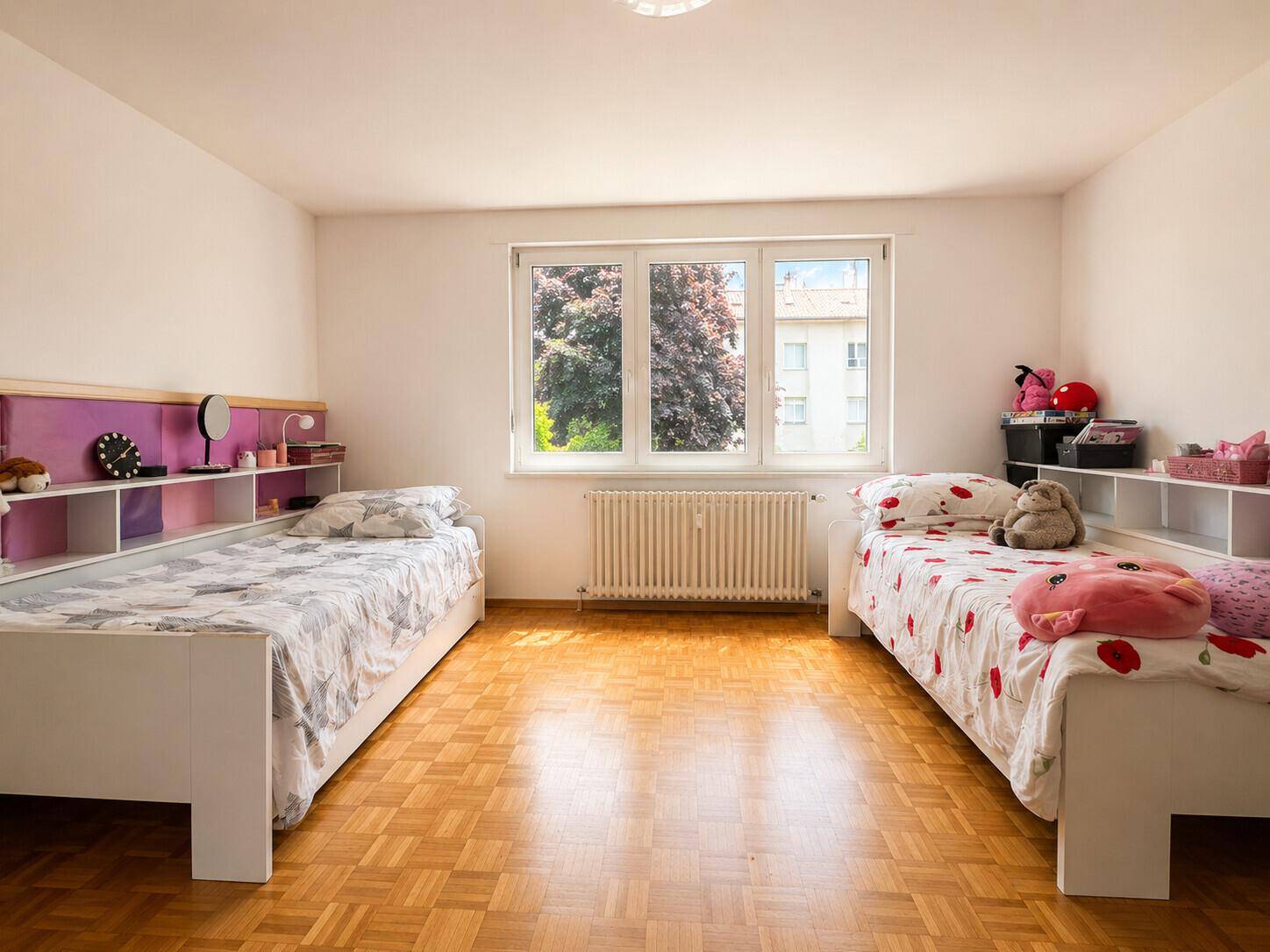 Kinderzimmer mit zwei Einzelbetten, Parkettboden und einem Fenster mit Blick ins Grüne.