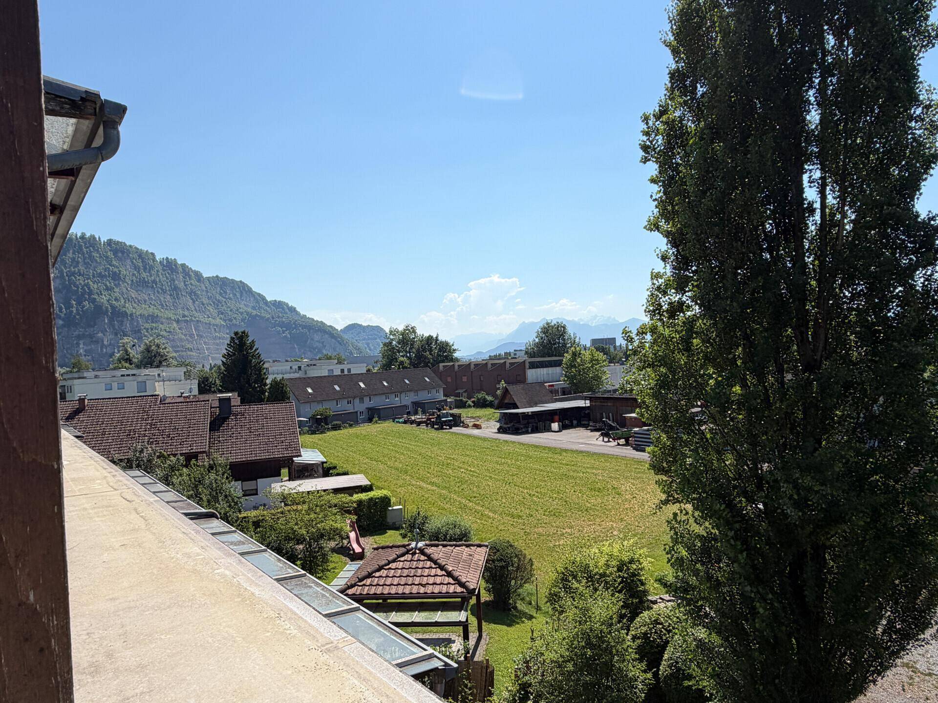 Panoramablick über Wohngebäude und grüne Flächen mit Bergen am Horizont.