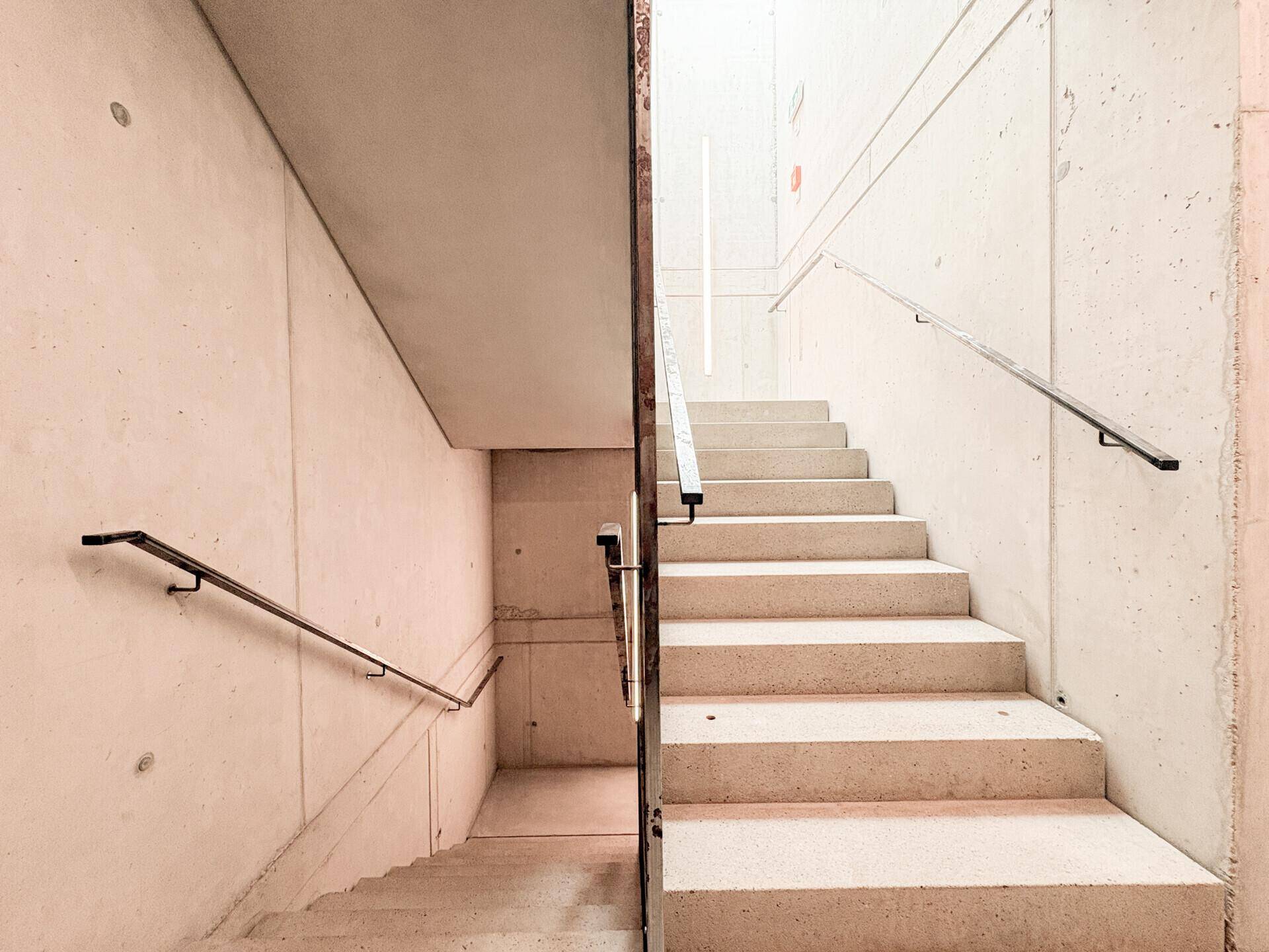 Moderner Treppenaufgang aus Beton mit schlichten Handläufen und klaren Linien.